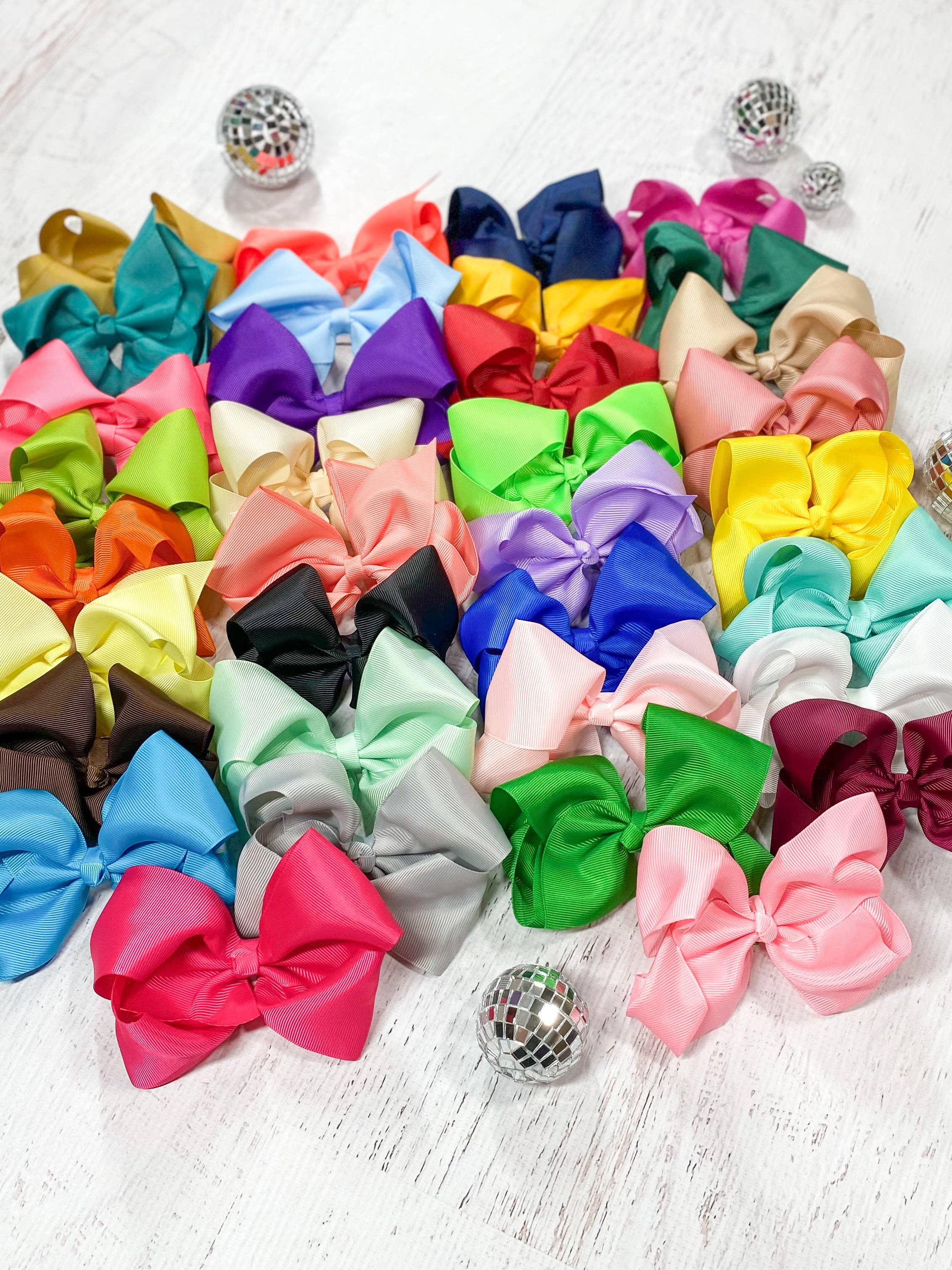 Assorted colorful hair bows on a light wooden surface with disco balls.