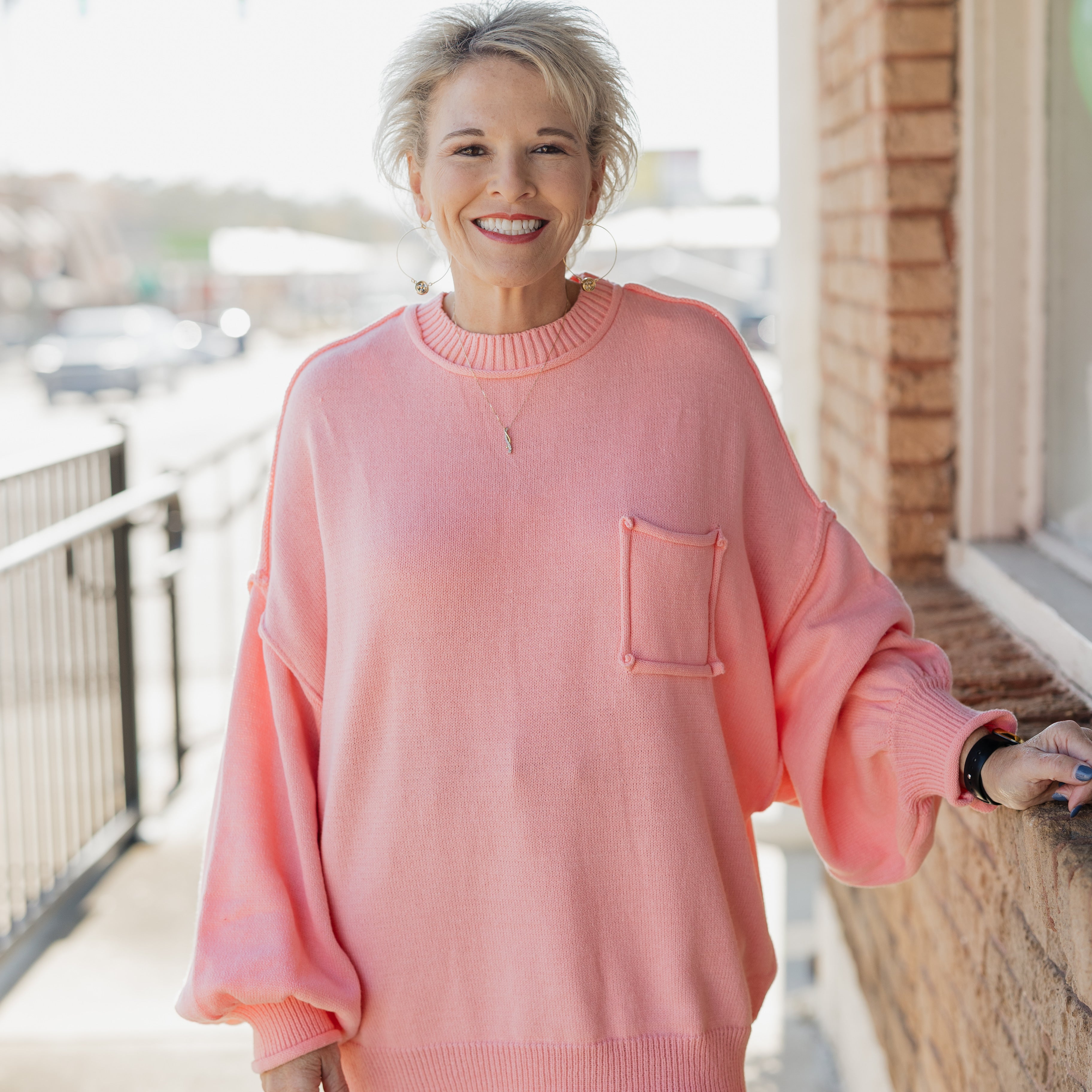 Person wearing a pink sweater with a pocket on a balcony