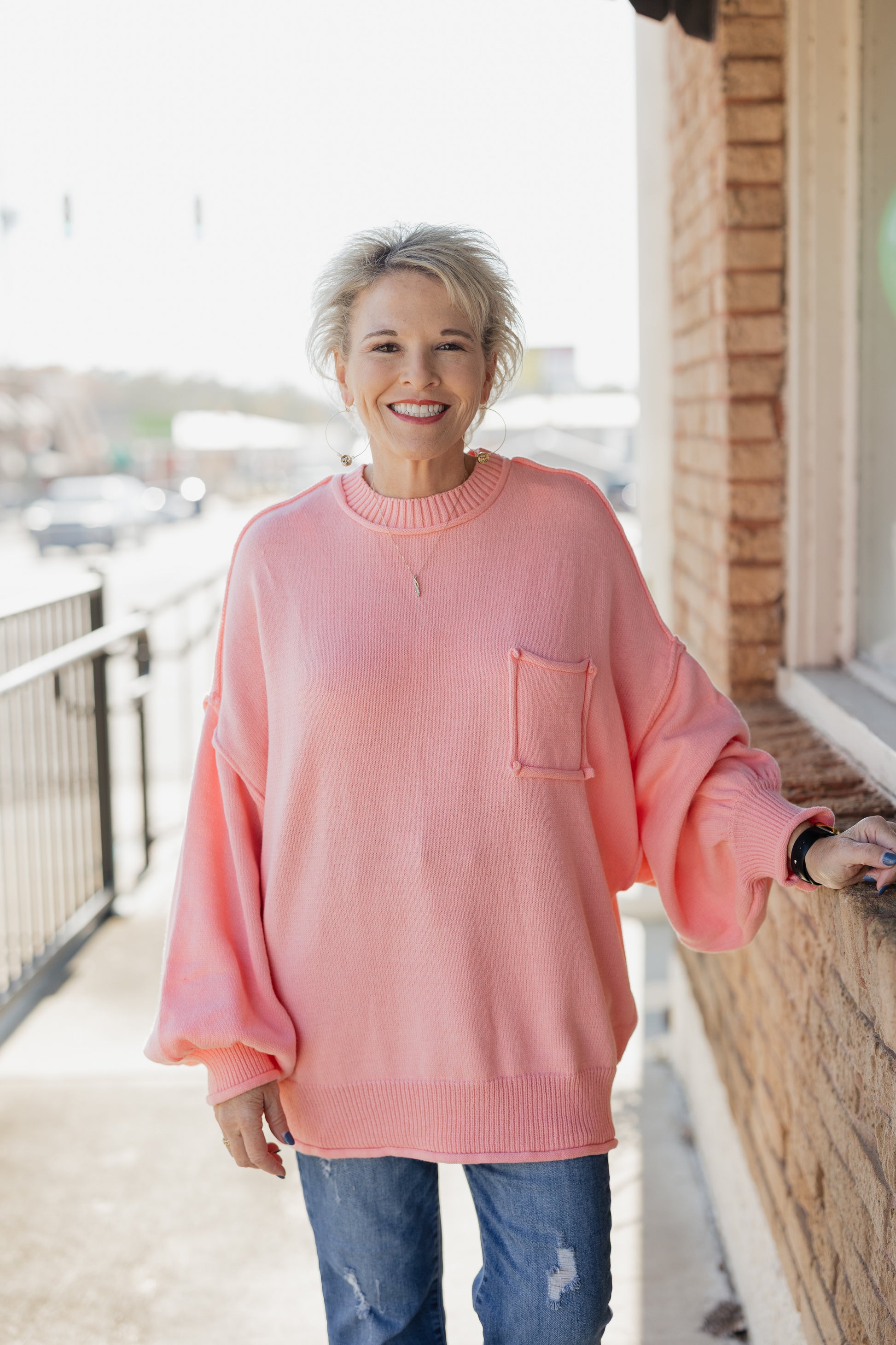 Person wearing a pink sweater with a pocket on a balcony