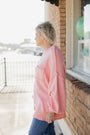 Person wearing a pink sweater standing by a window with a blurred background