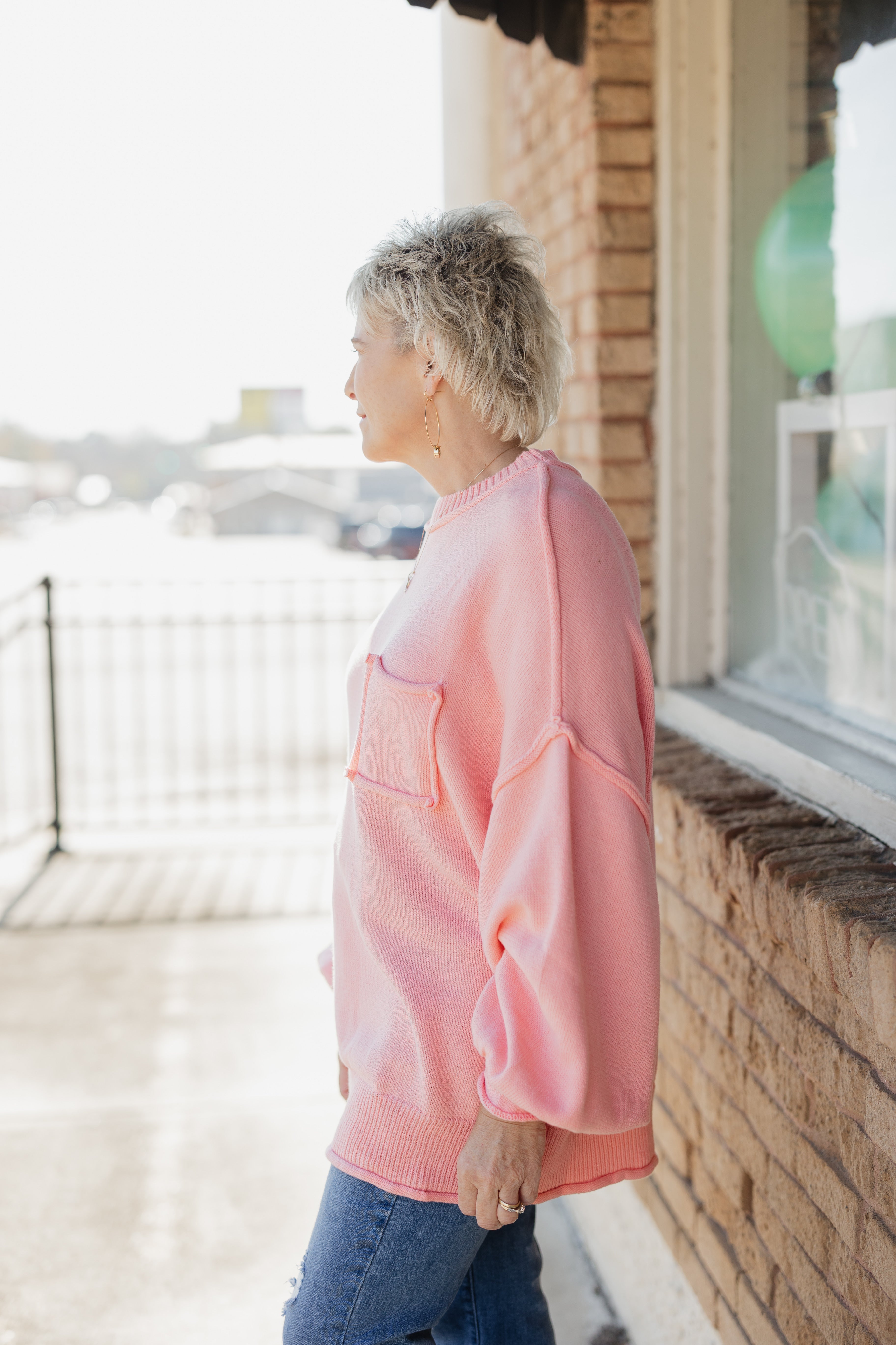 Person wearing a pink sweater standing by a window with a blurred background