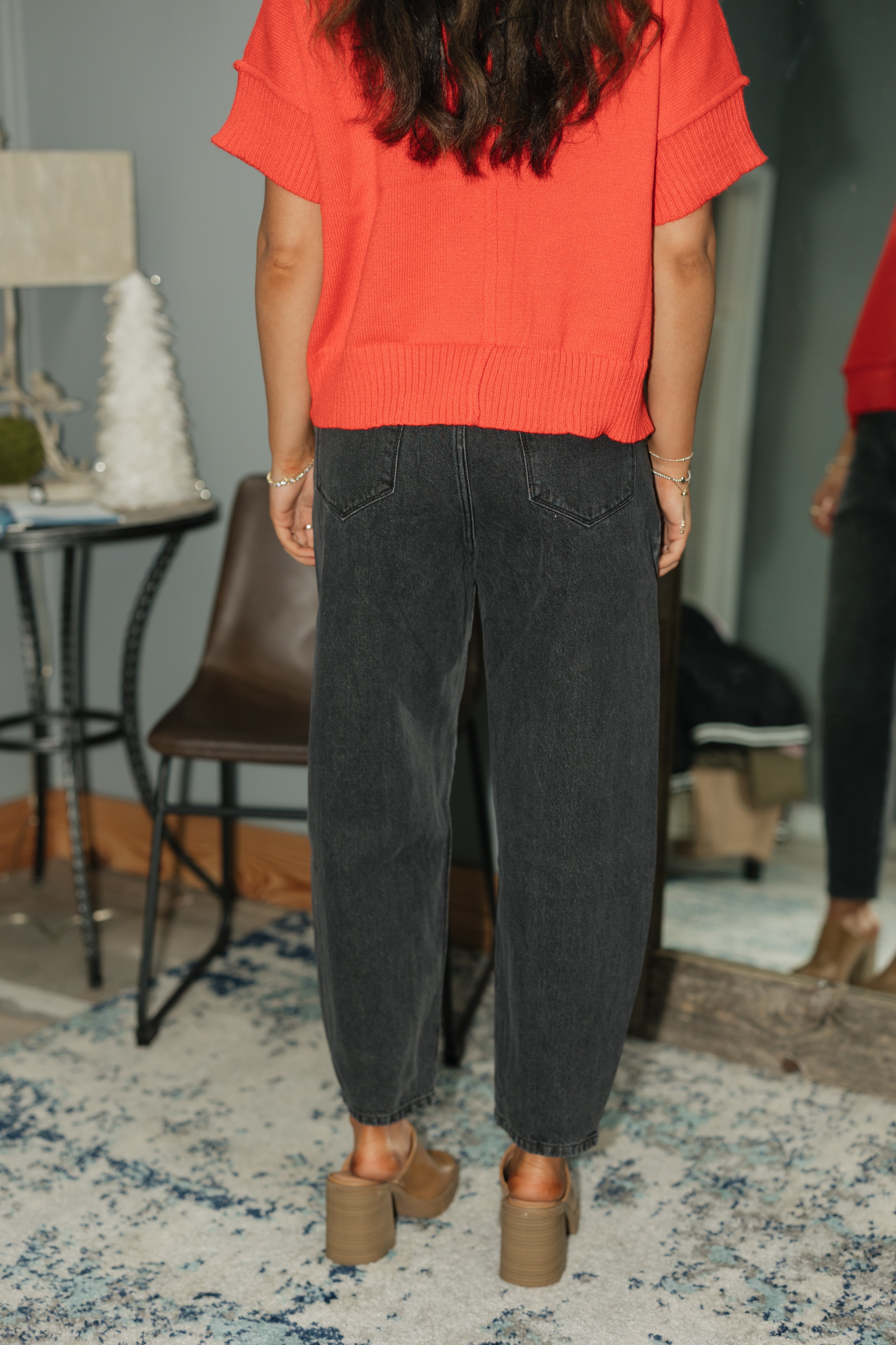 Person wearing a red top and black pants standing on a patterned rug.