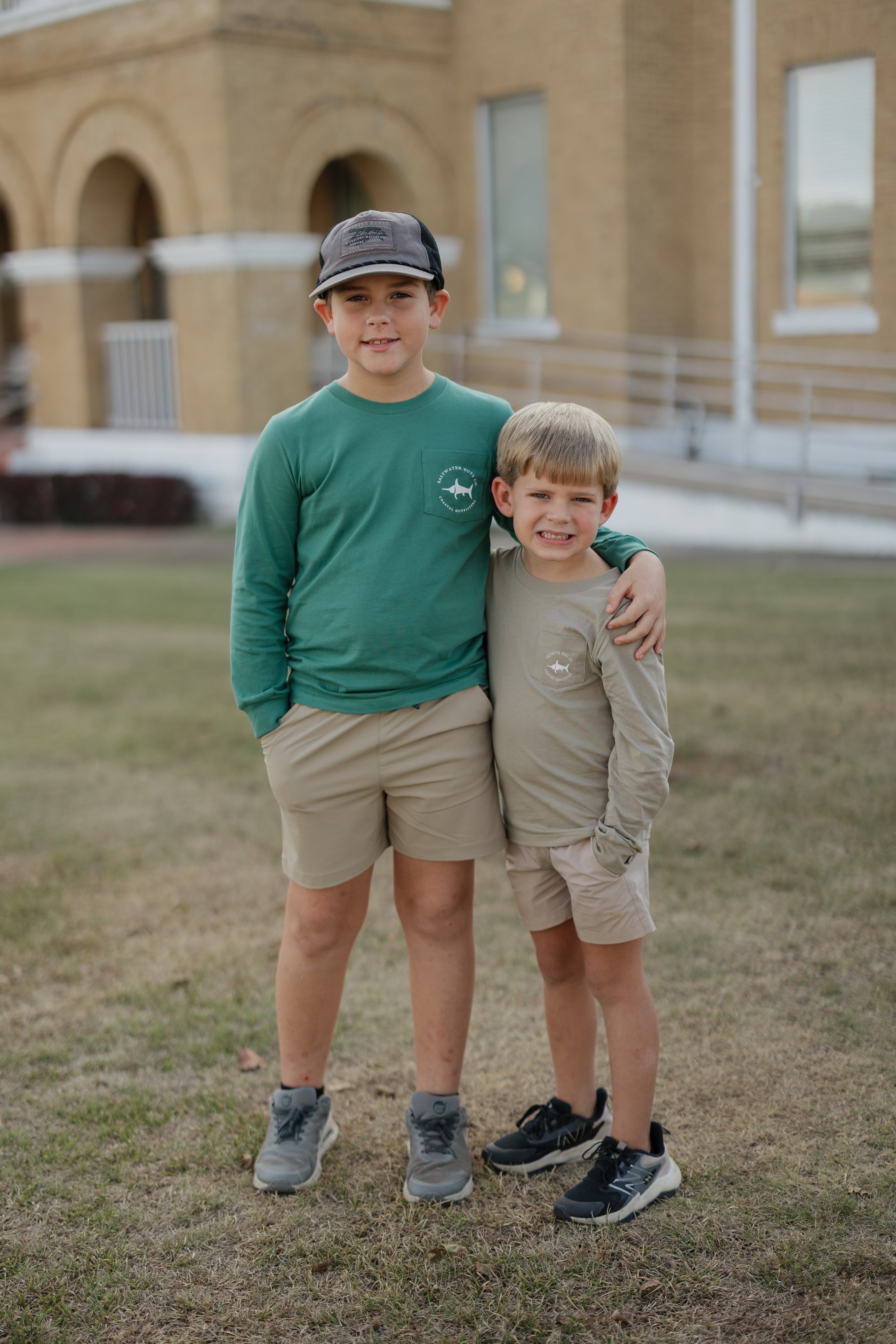 Two boys standing together on grass with a building in the background