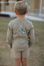 Child wearing a long-sleeve shirt with a graphic design on the back, standing outdoors.