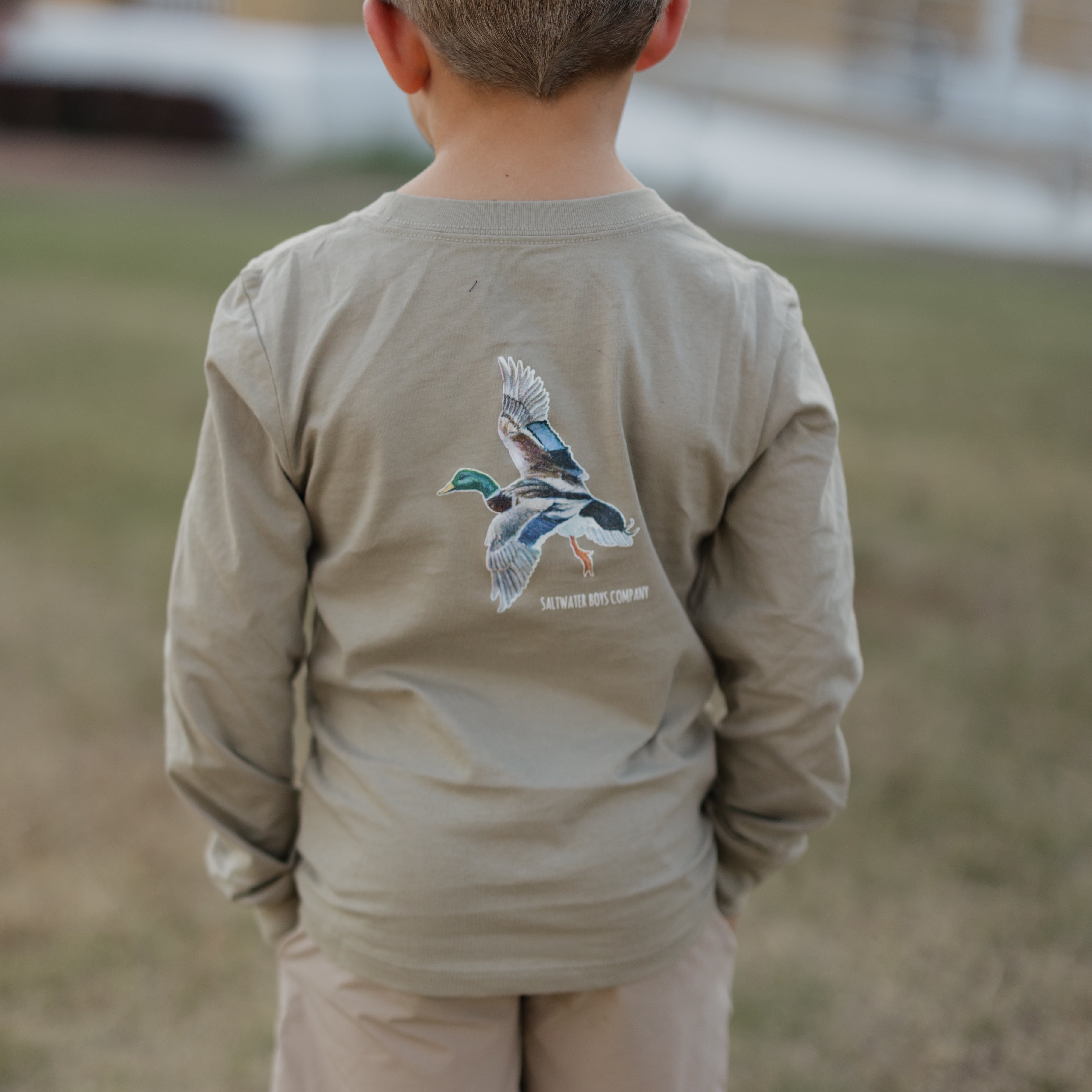 Child wearing a long-sleeve shirt with a graphic design on the back, standing outdoors.