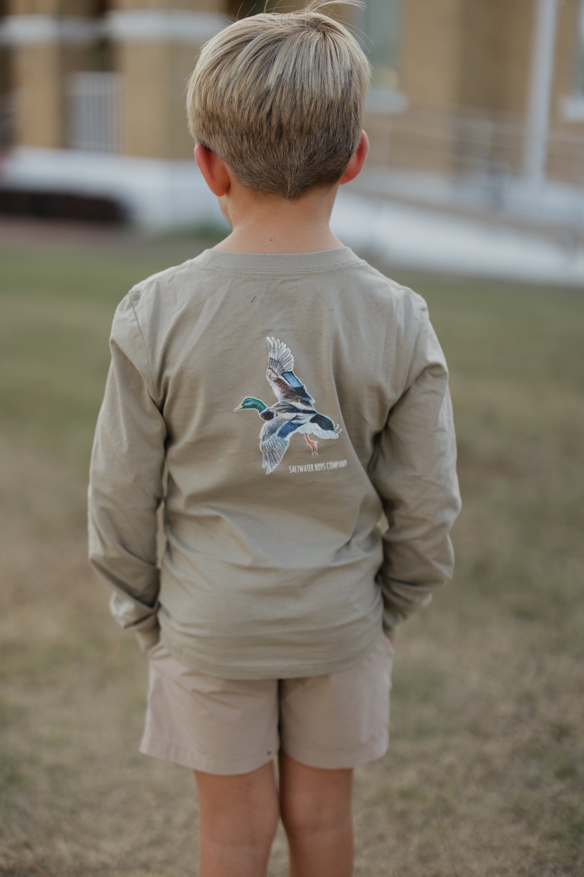 Child wearing a long-sleeve shirt with a graphic design on the back, standing outdoors.