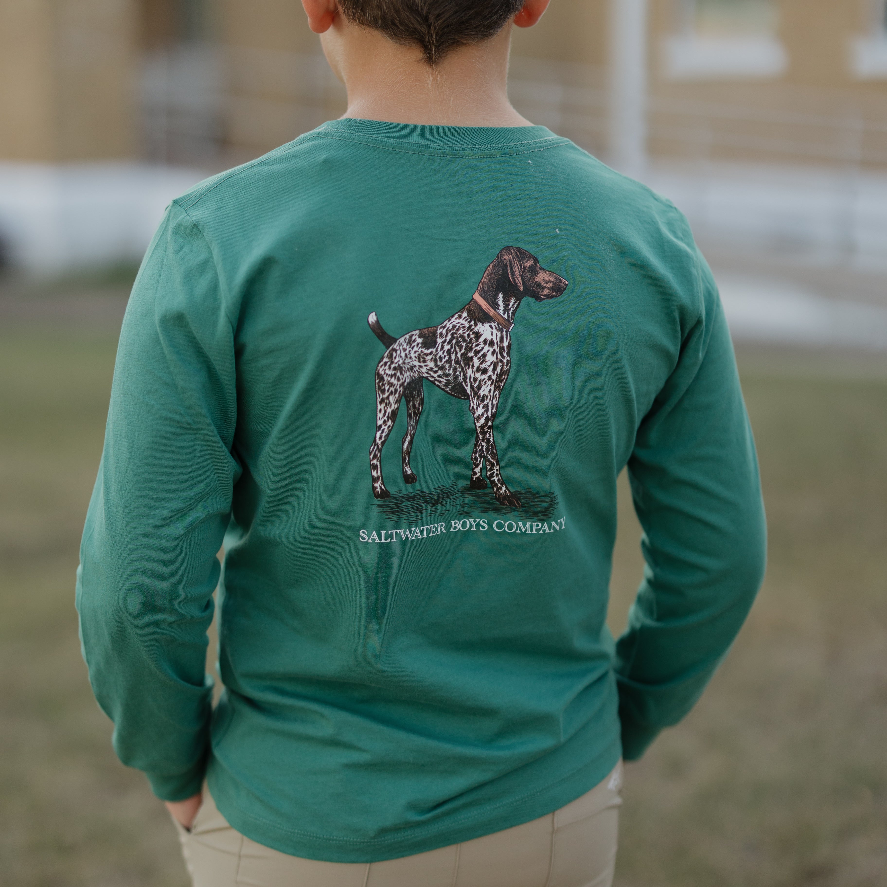 Person wearing a green long-sleeve shirt with a dog illustration and text, standing outdoors.