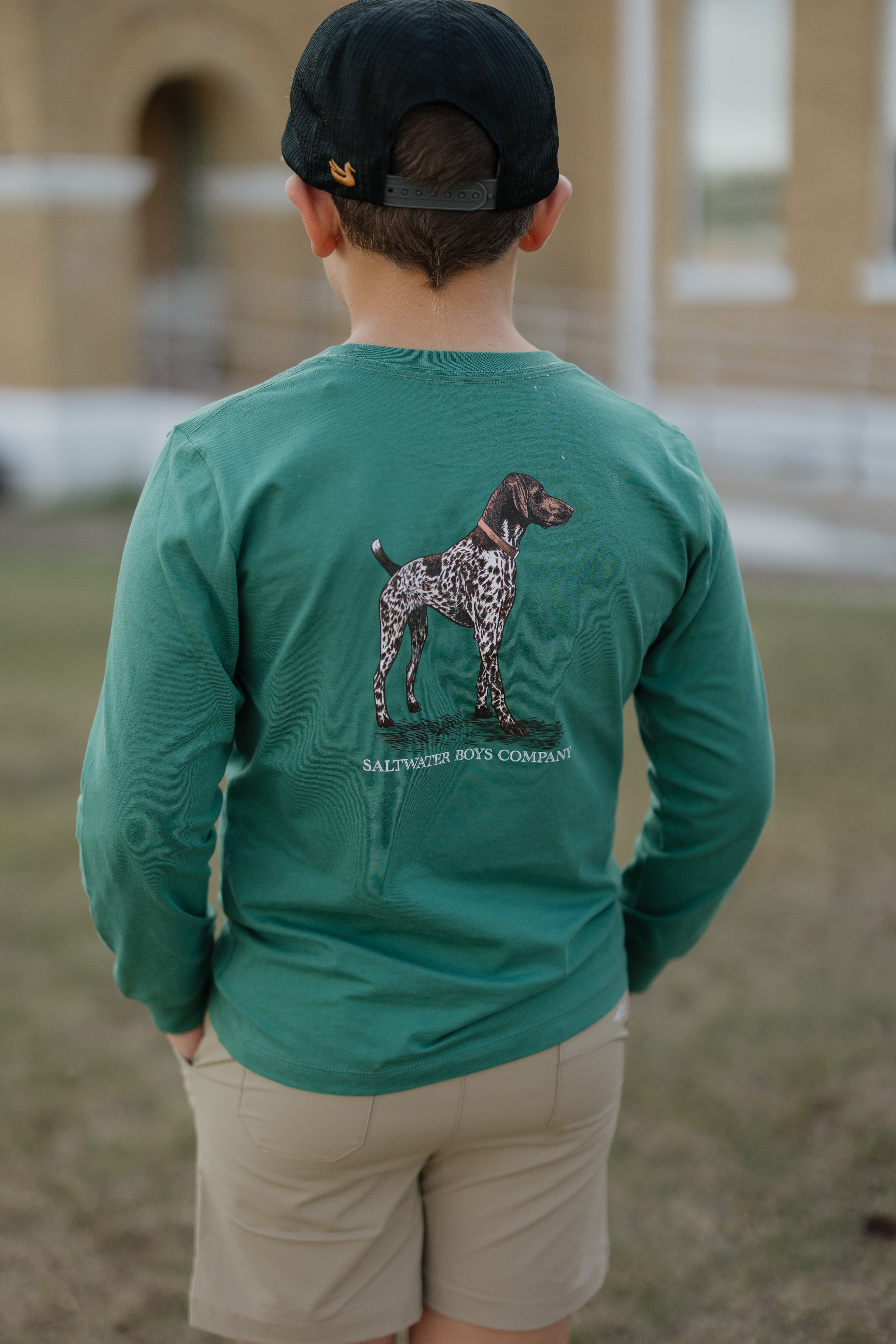 Person wearing a green long-sleeve shirt with a dog illustration and text, standing outdoors.