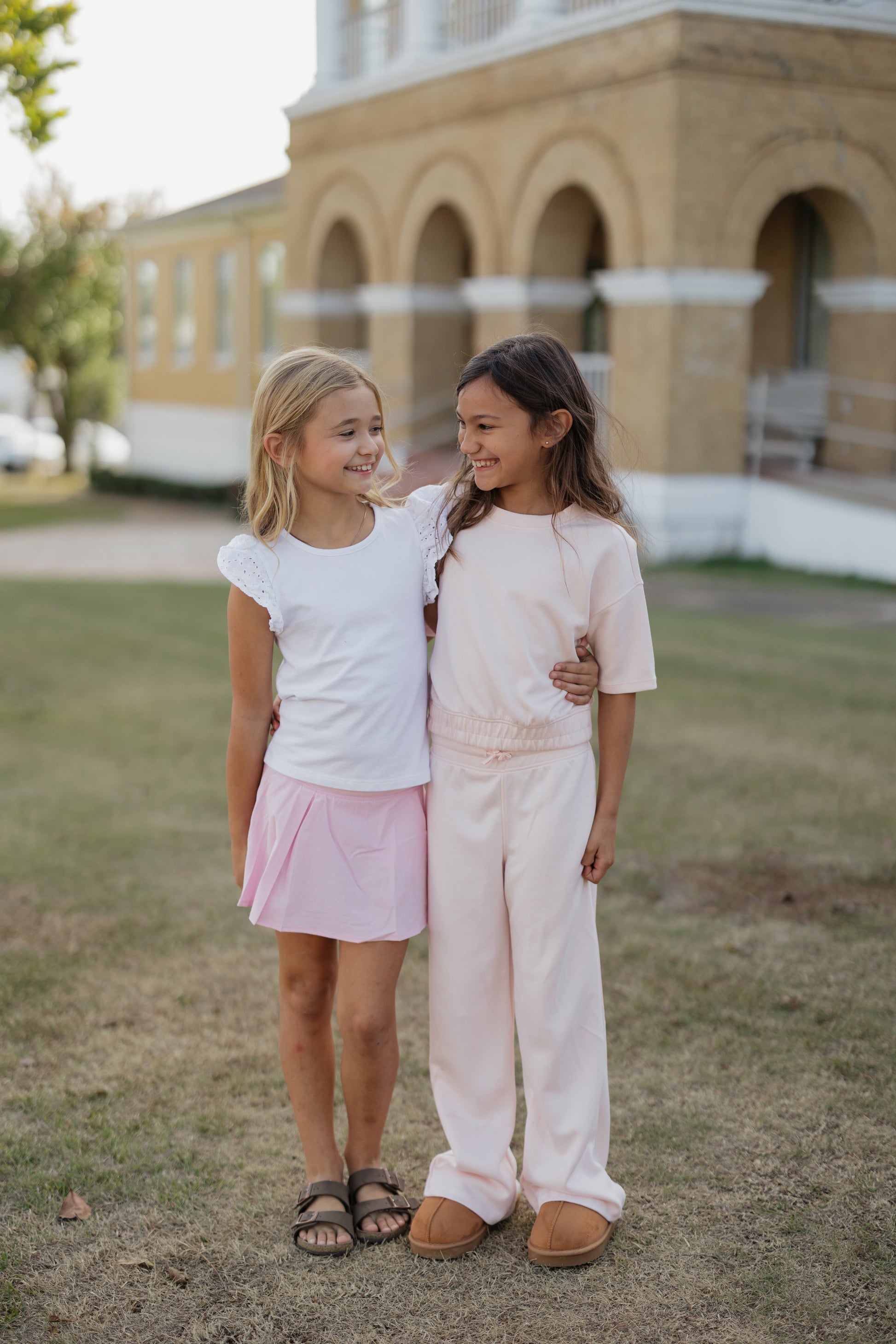 Two young girls standing together in front of a building with arches.