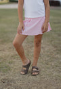 Person wearing a pink skirt and brown sandals on a grassy background