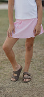Person wearing a pink skirt and brown sandals on a grassy background