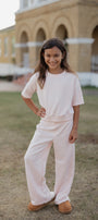 Young girl in a light pink outfit standing outdoors with a building in the background