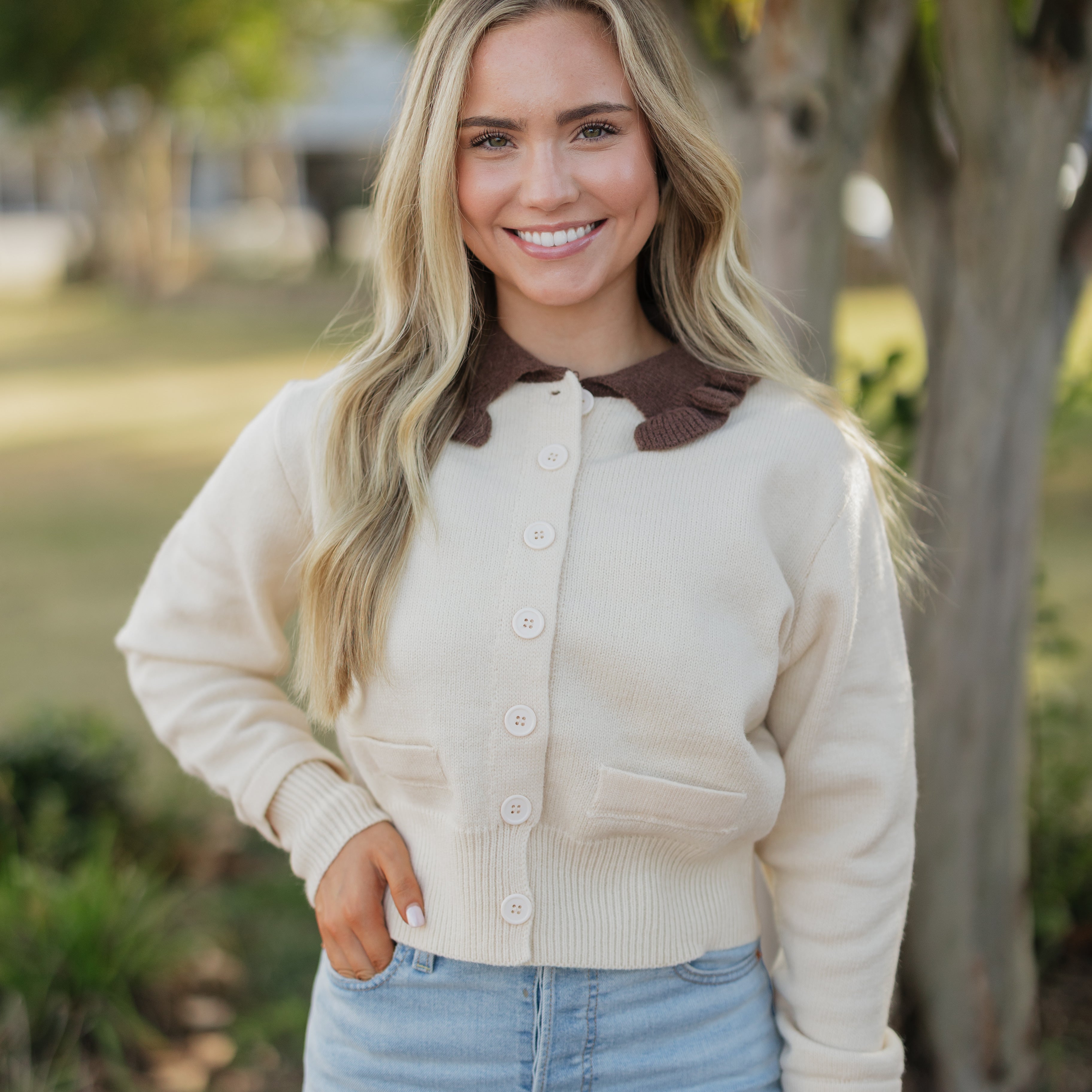 Woman wearing a cream cardigan with a brown collar in an outdoor setting