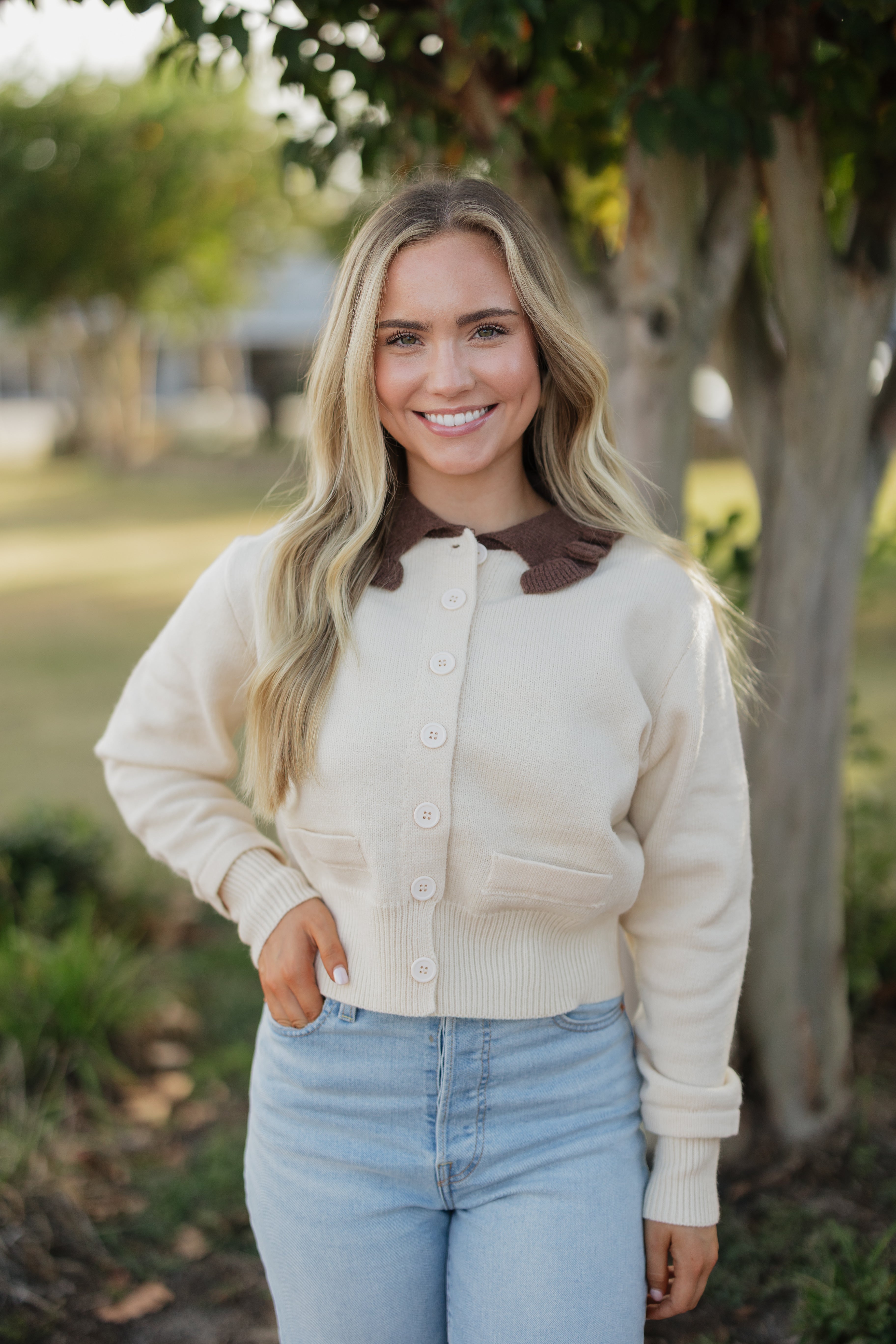 Woman wearing a cream cardigan with a brown collar in an outdoor setting