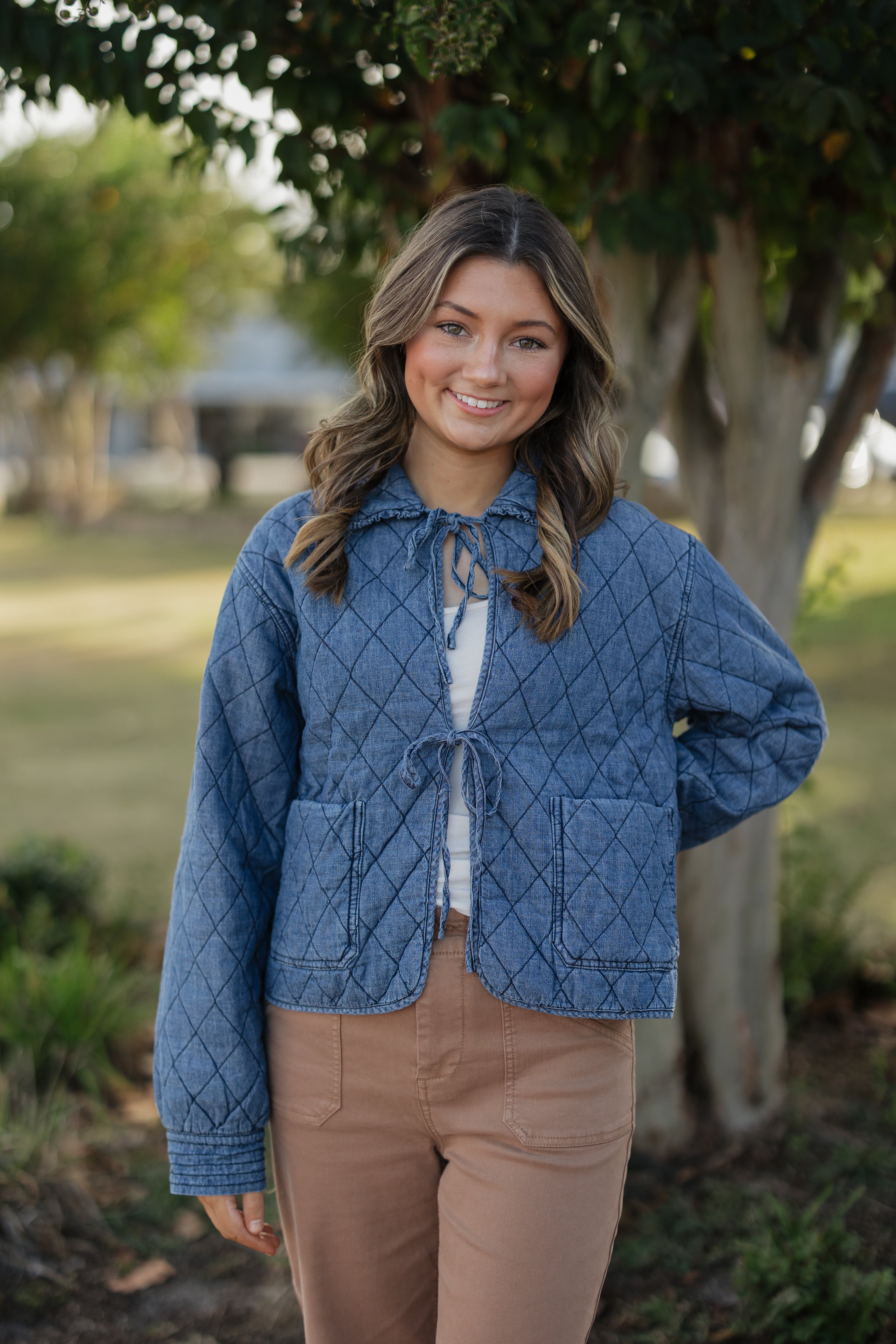 Woman wearing a blue quilted jacket outdoors with trees in the background