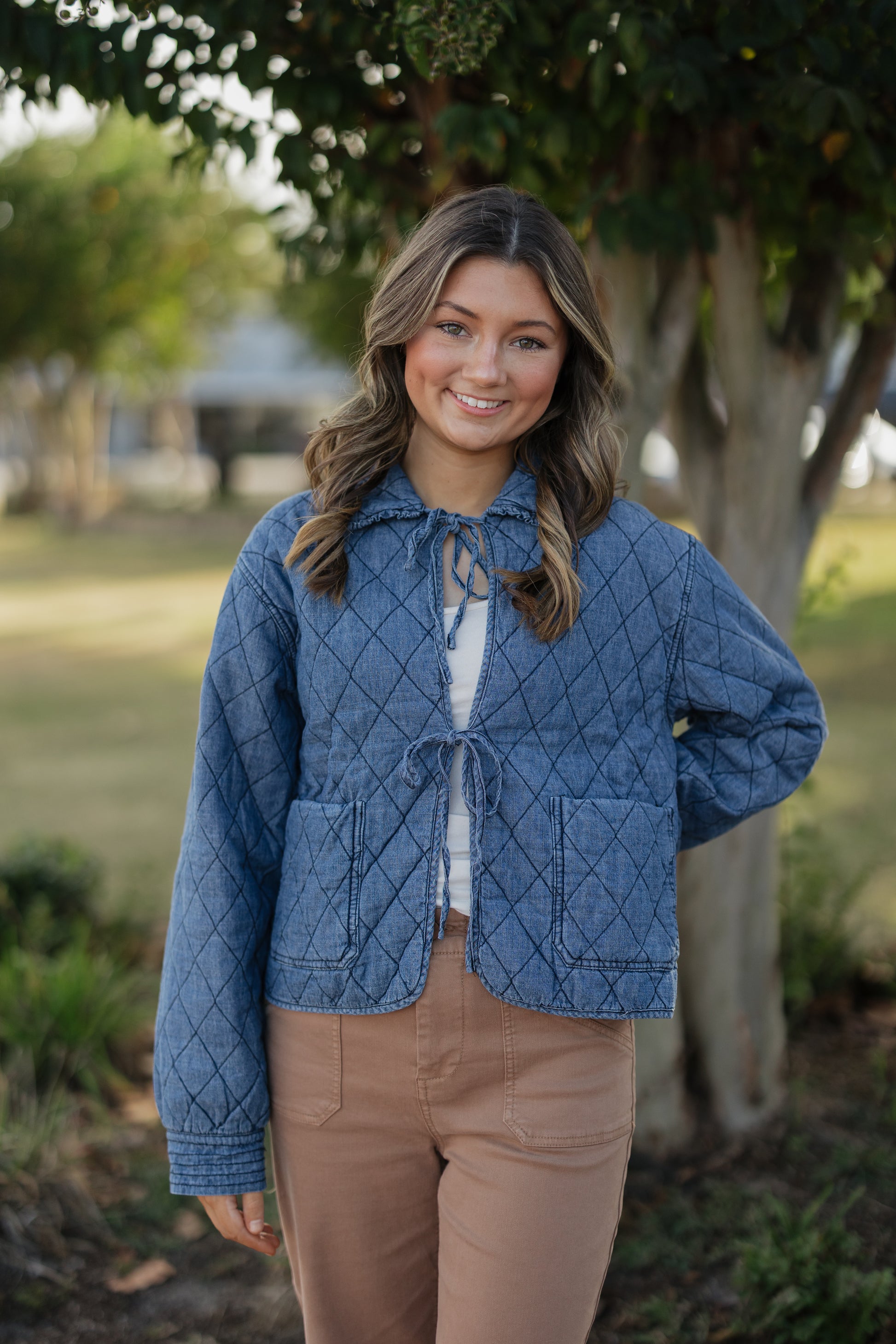 Woman wearing a blue quilted jacket outdoors with trees in the background