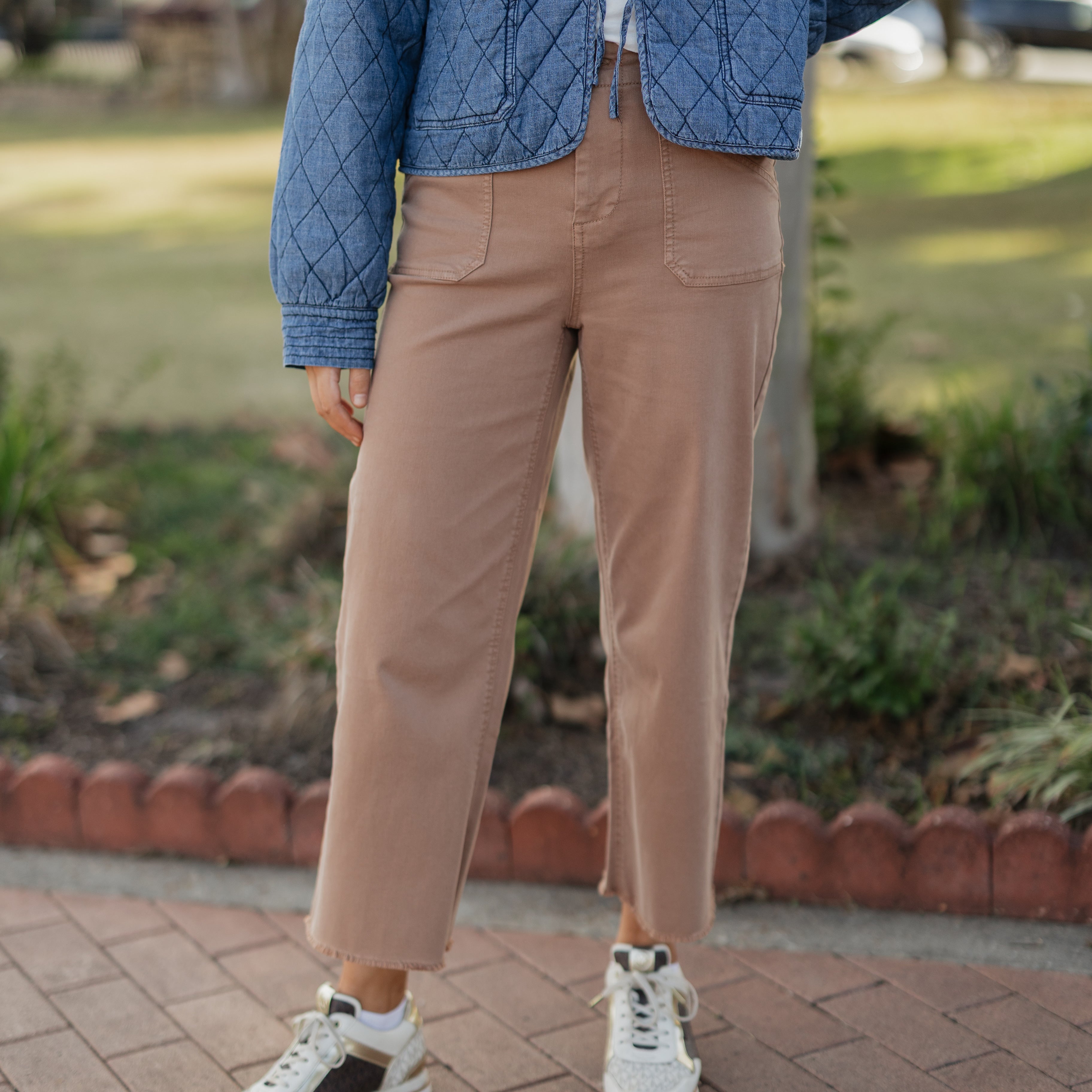 Person wearing a blue quilted jacket, beige pants, and white sneakers on a paved walkway.