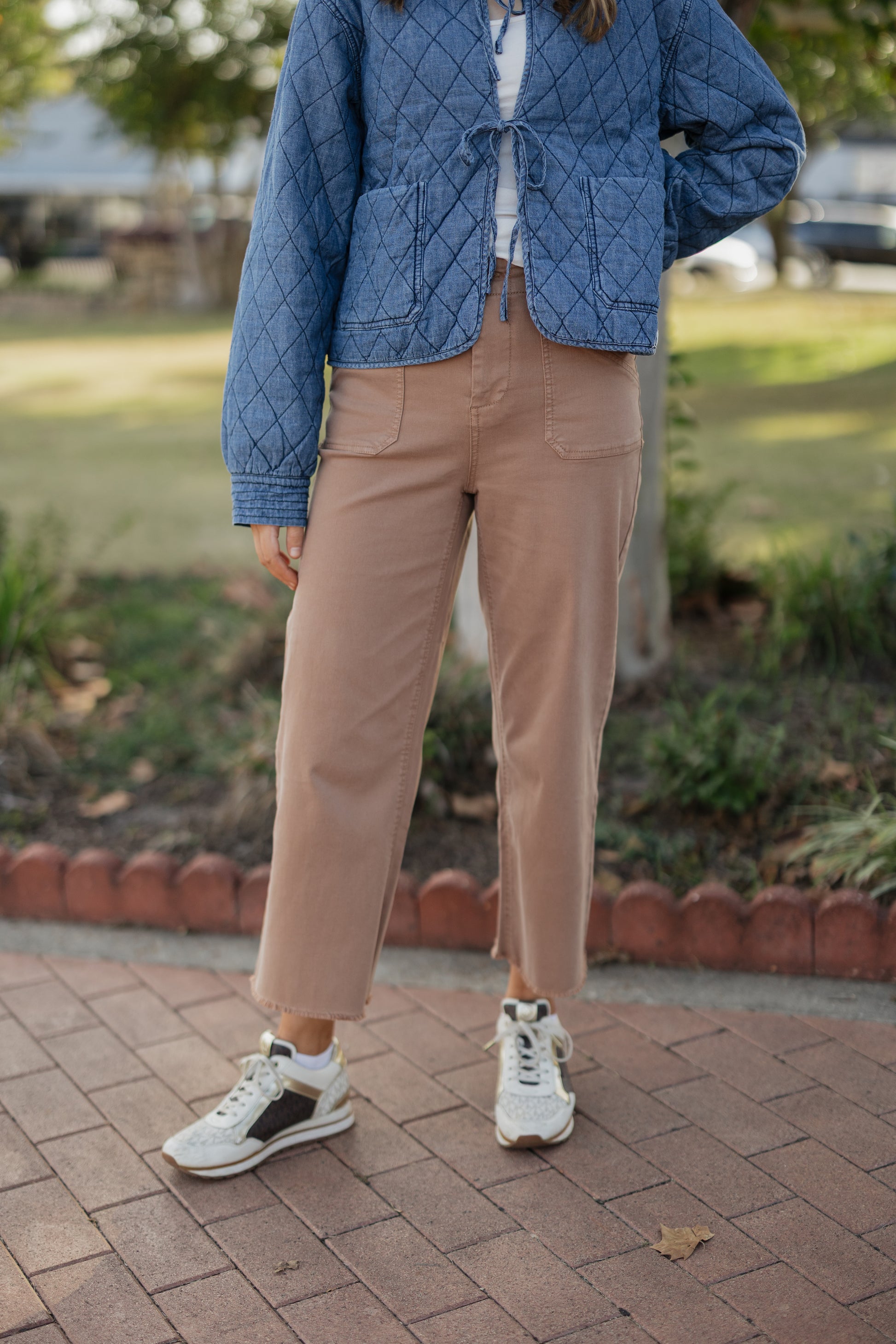 Person wearing a blue quilted jacket, beige pants, and white sneakers on a paved walkway.