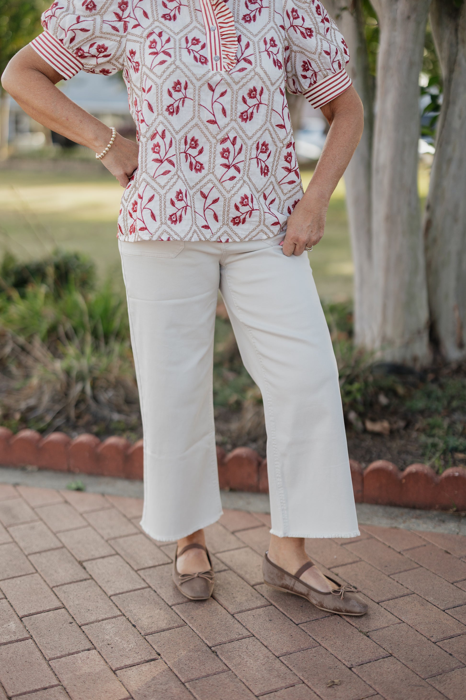 Person wearing a red and white patterned top with khaki pants on a paved walkway.