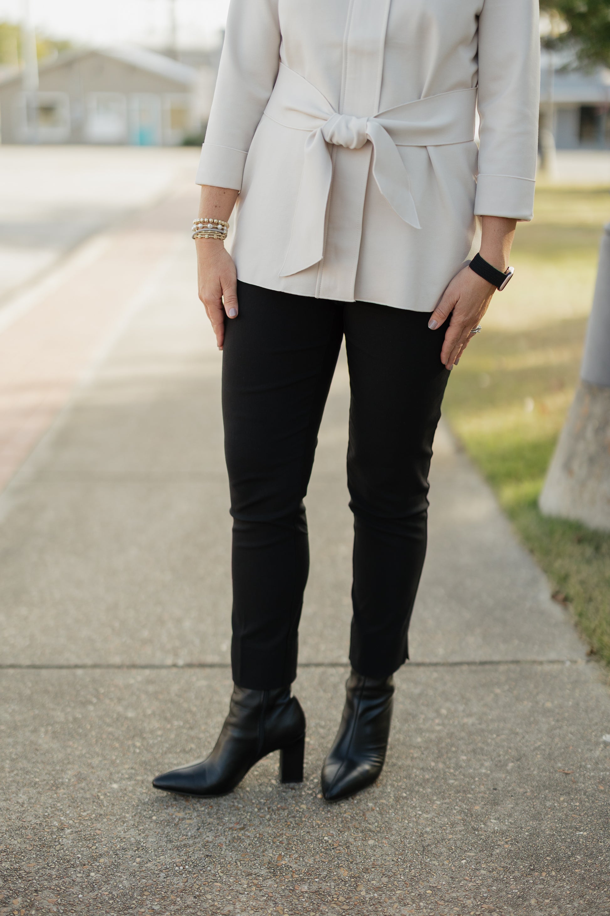 Person wearing a beige blazer, black pants, and black boots on a sidewalk.