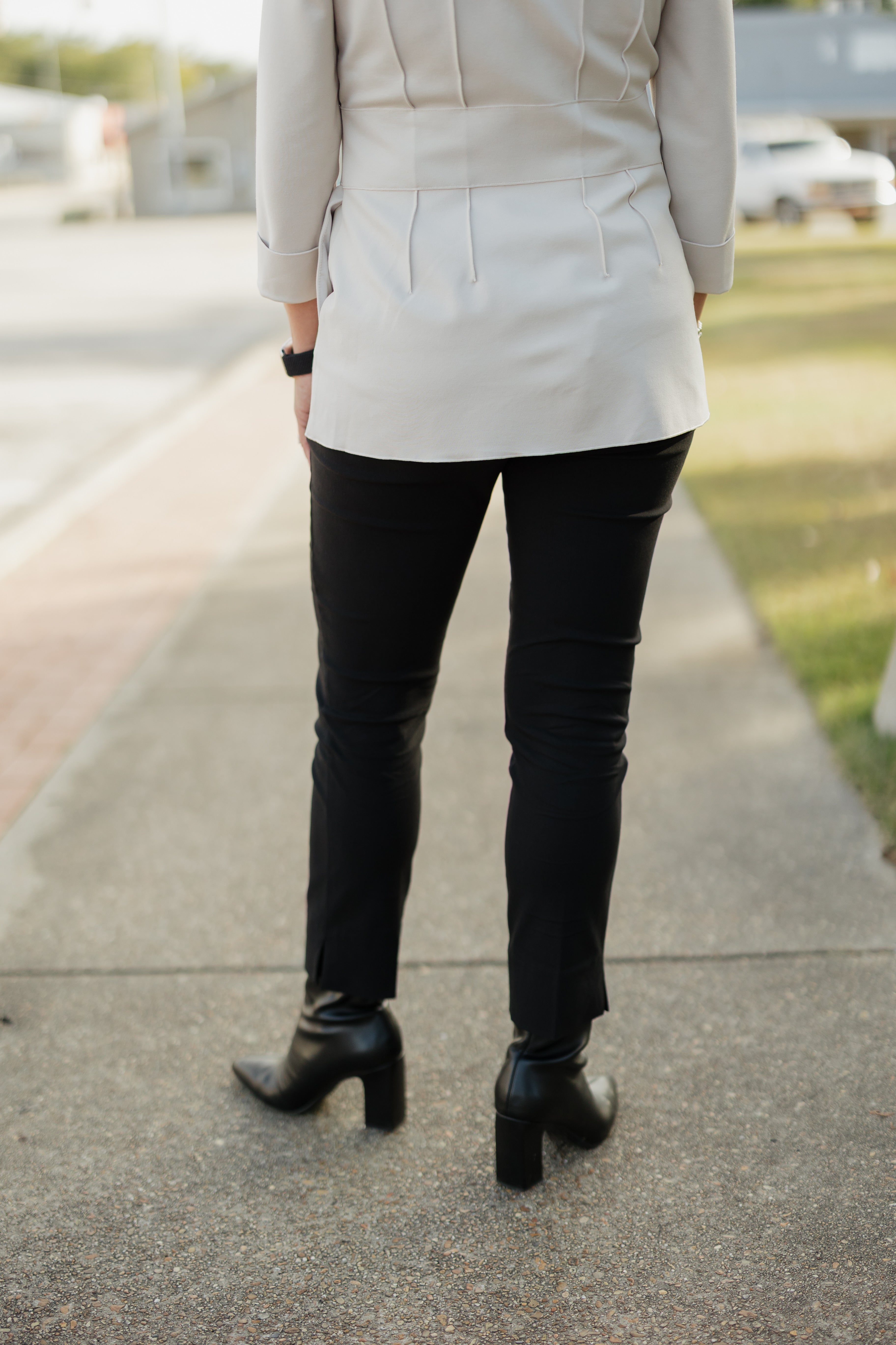 Person wearing a light-colored blazer, black pants, and black boots on a sidewalk.