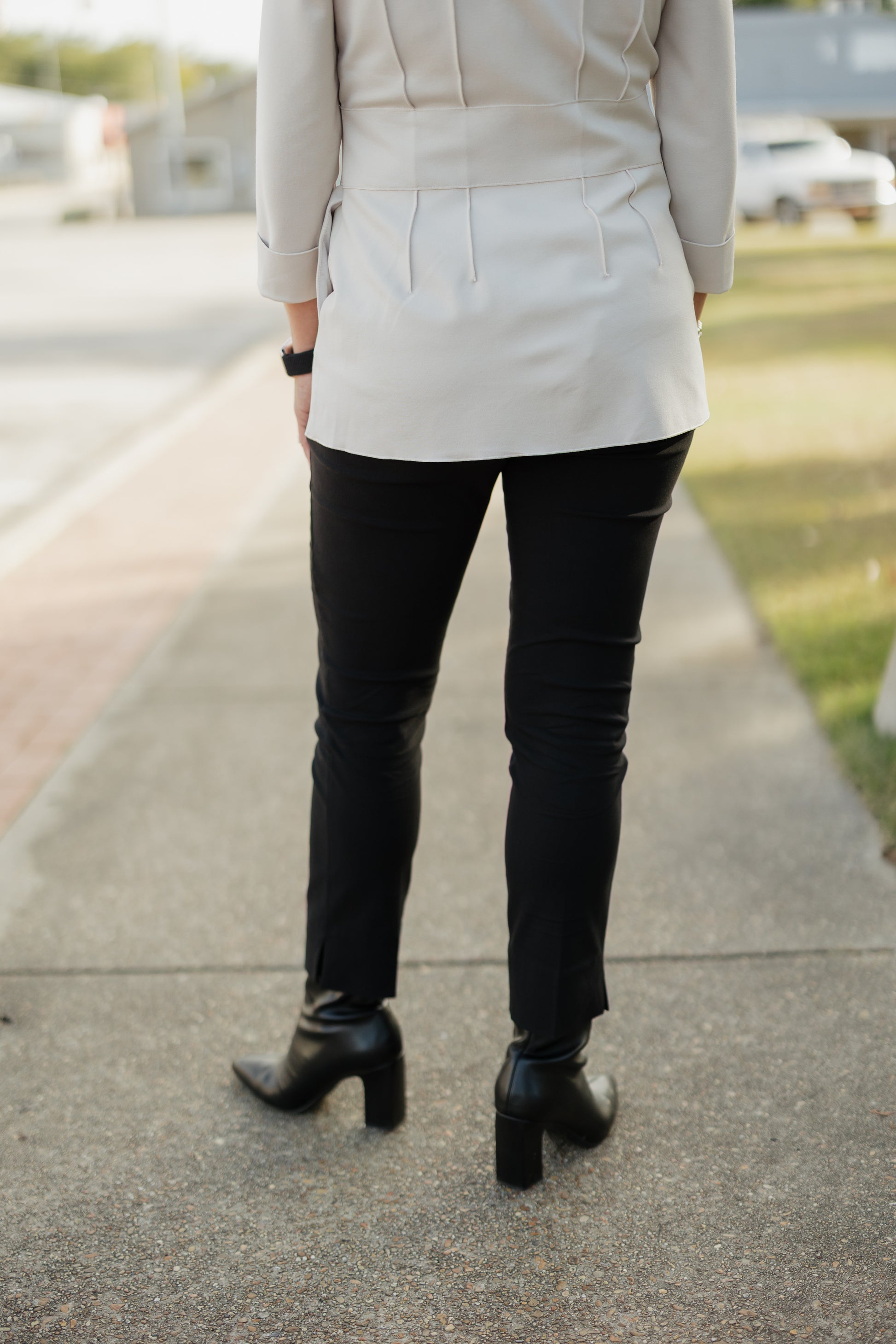 Person wearing a light-colored blazer, black pants, and black boots on a sidewalk.