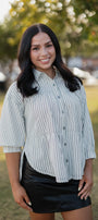 Woman wearing a striped shirt and black skirt standing outdoors with trees and cars in the background