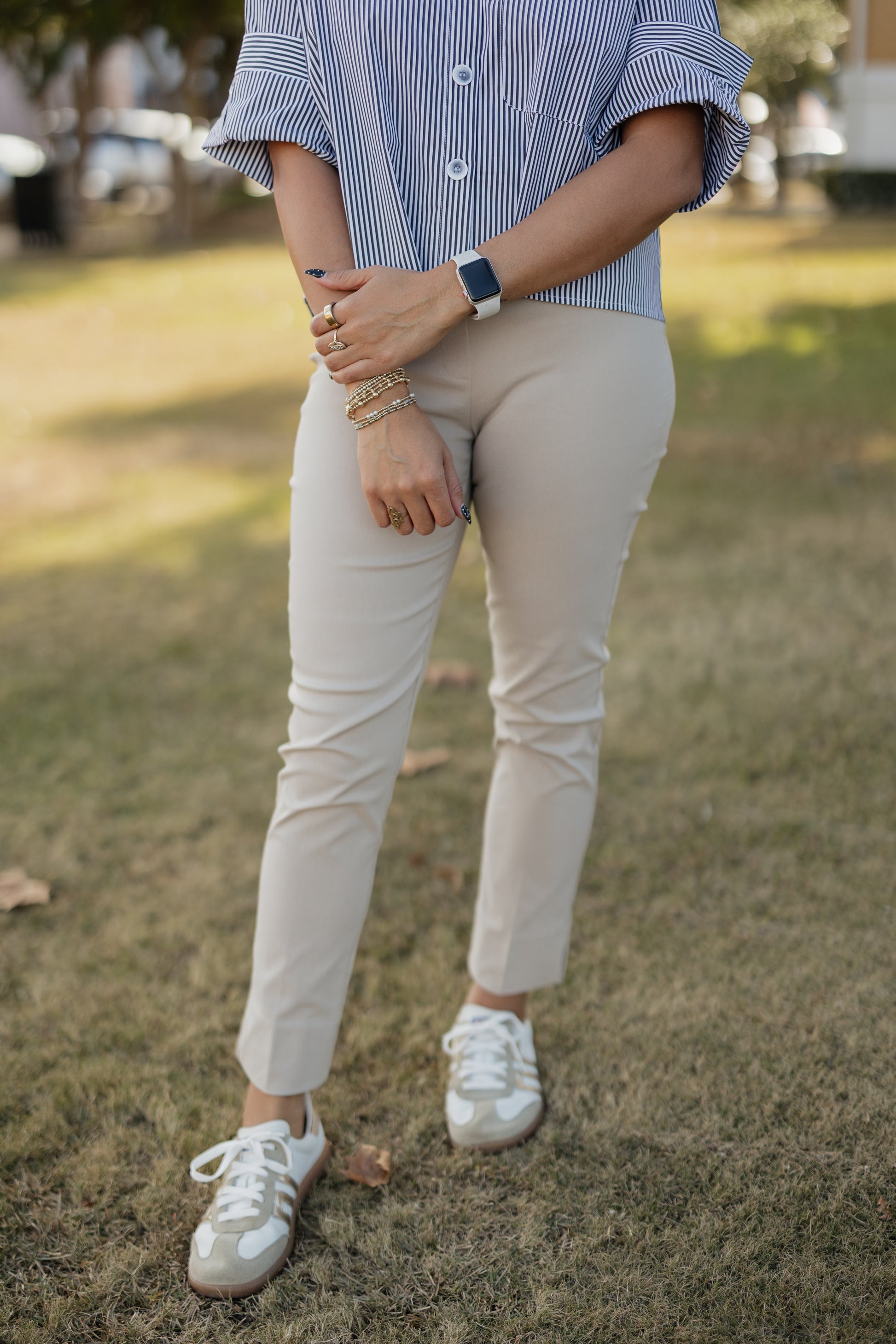 Person wearing a blue and white striped shirt, beige pants, and white sneakers on grass.