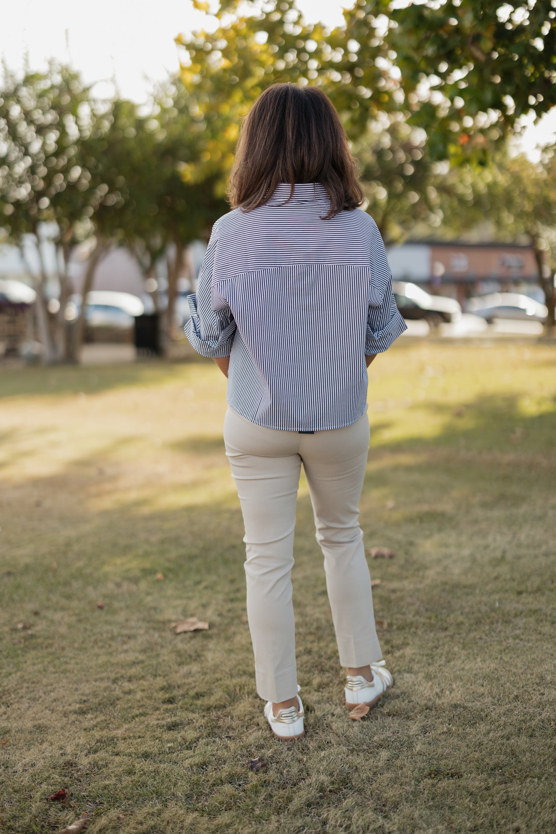 Person wearing a blue striped shirt and white pants standing on grass with trees in the background