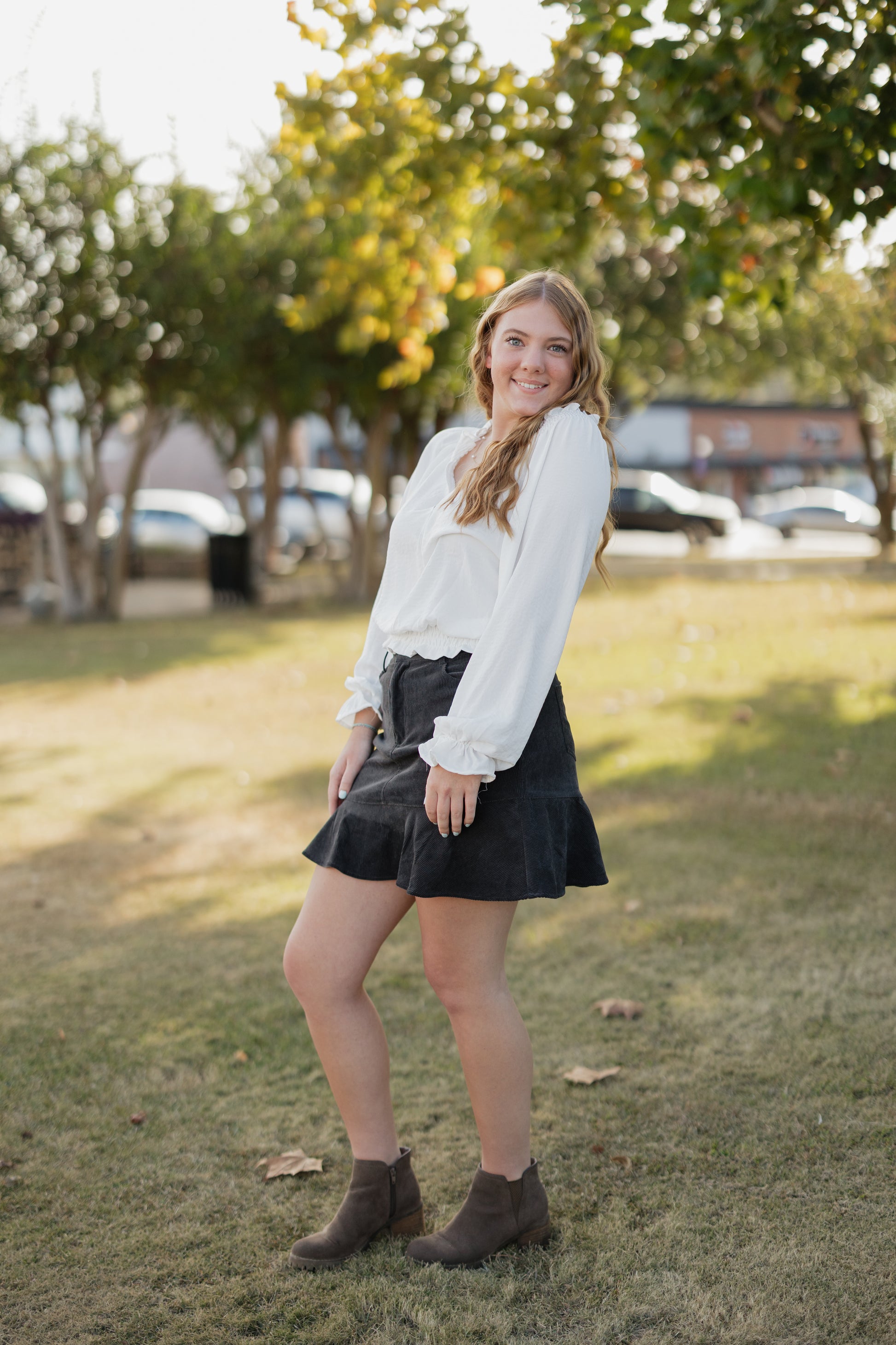 Woman in a white blouse and black skirt standing in a park.