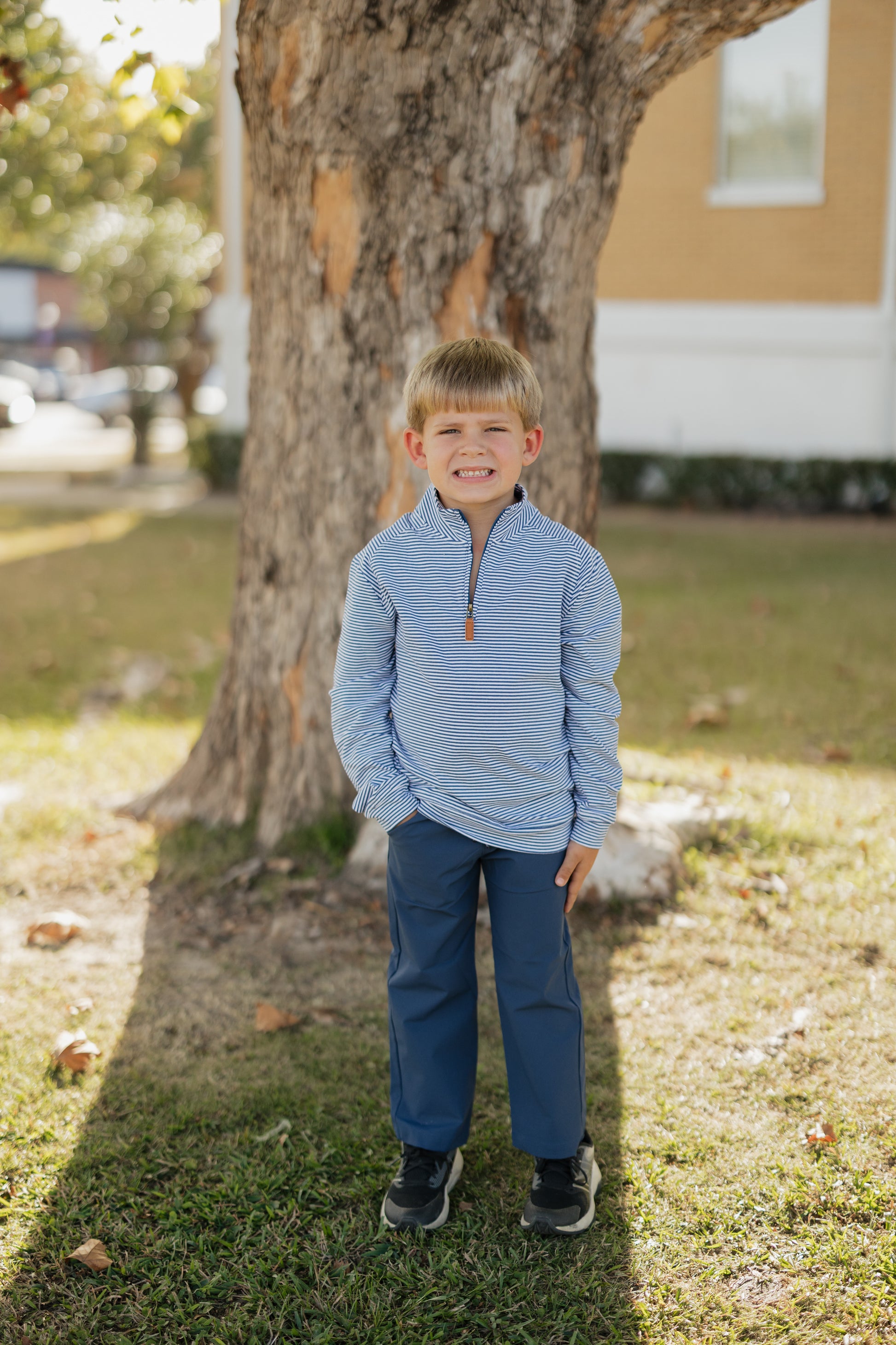 Young boy in a blue outfit standing in front of a tree