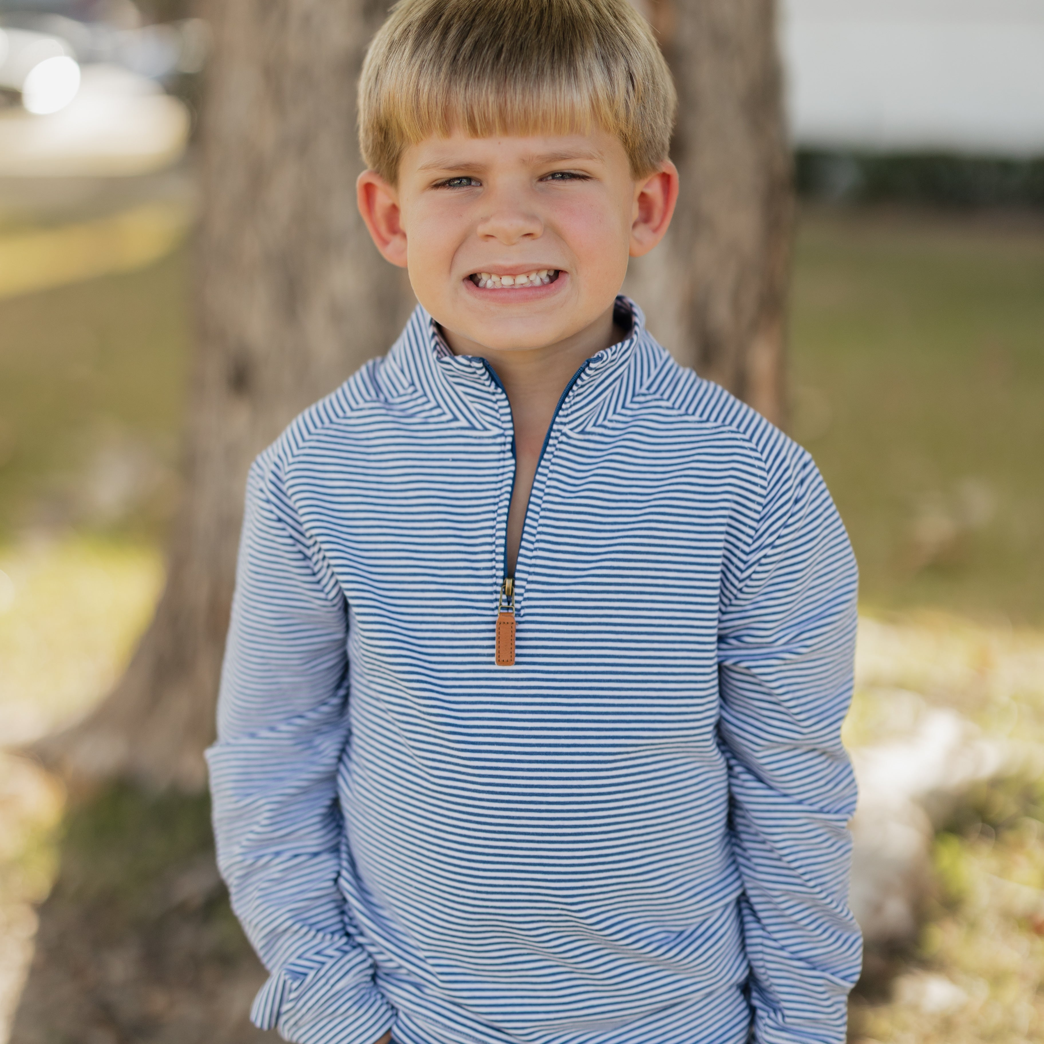 Young boy wearing a blue striped shirt standing outdoors near a tree