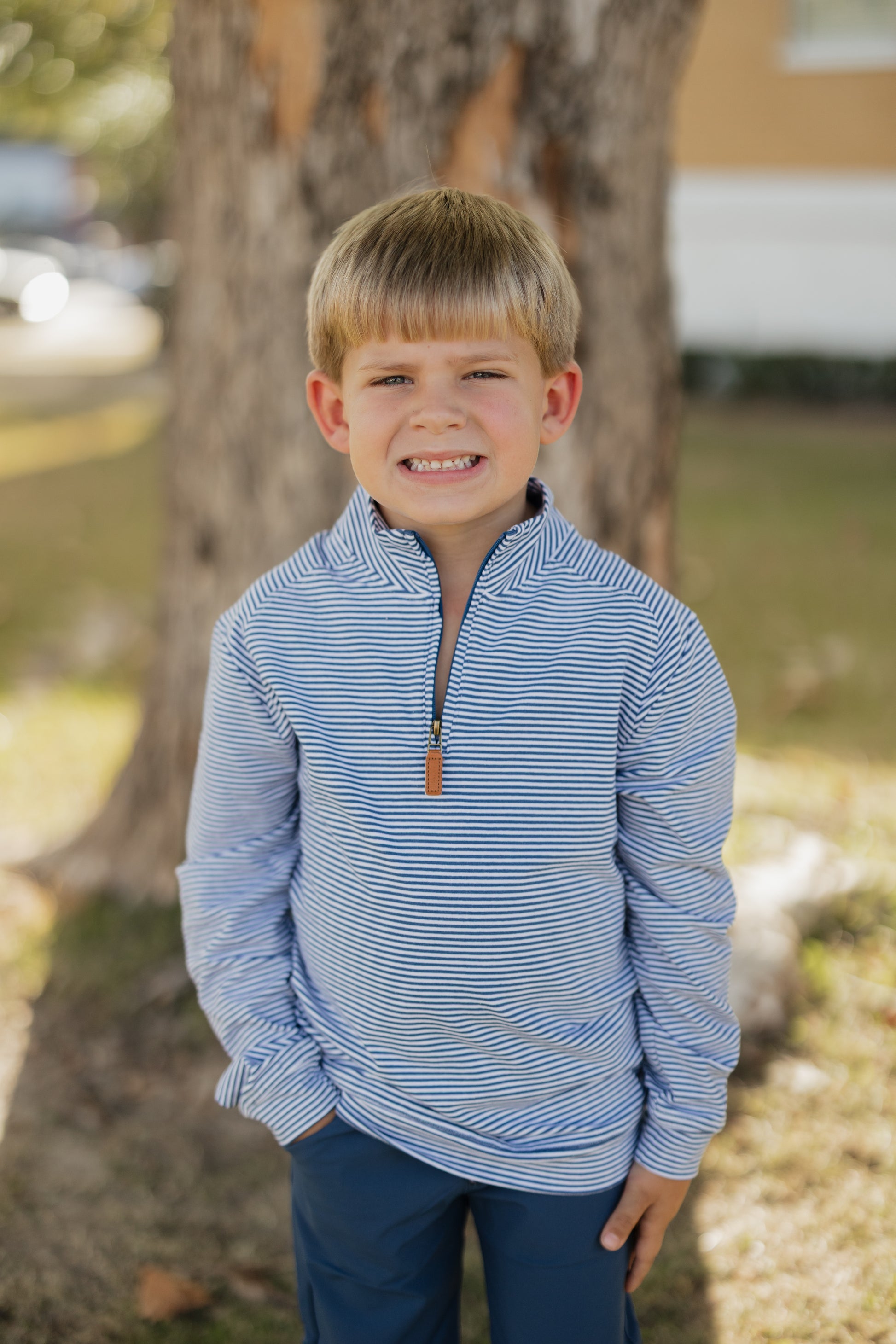 Young boy wearing a blue striped shirt standing outdoors near a tree