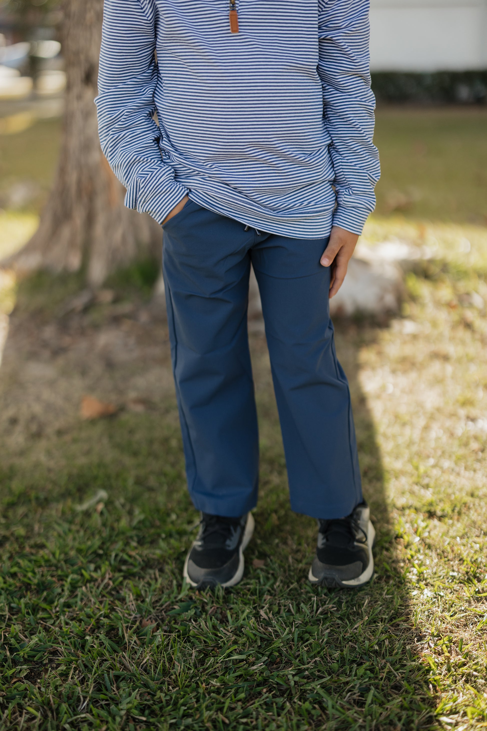 Person wearing a striped shirt and blue pants standing on grass