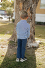 Child in a striped shirt and blue pants standing next to a tree