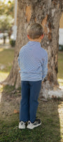 Child in a striped shirt and blue pants standing next to a tree