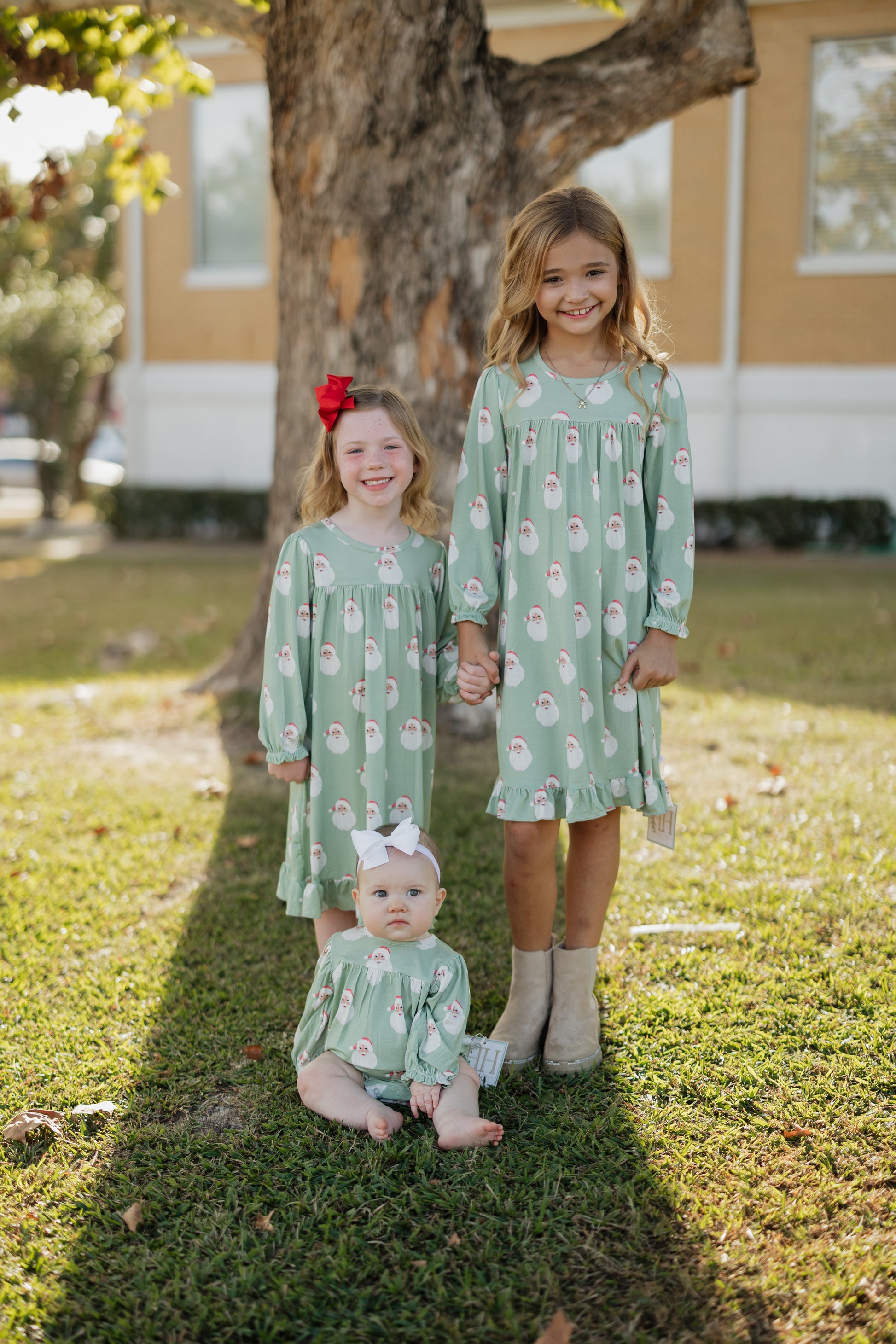 Three children in matching green dresses standing outdoors on grass.