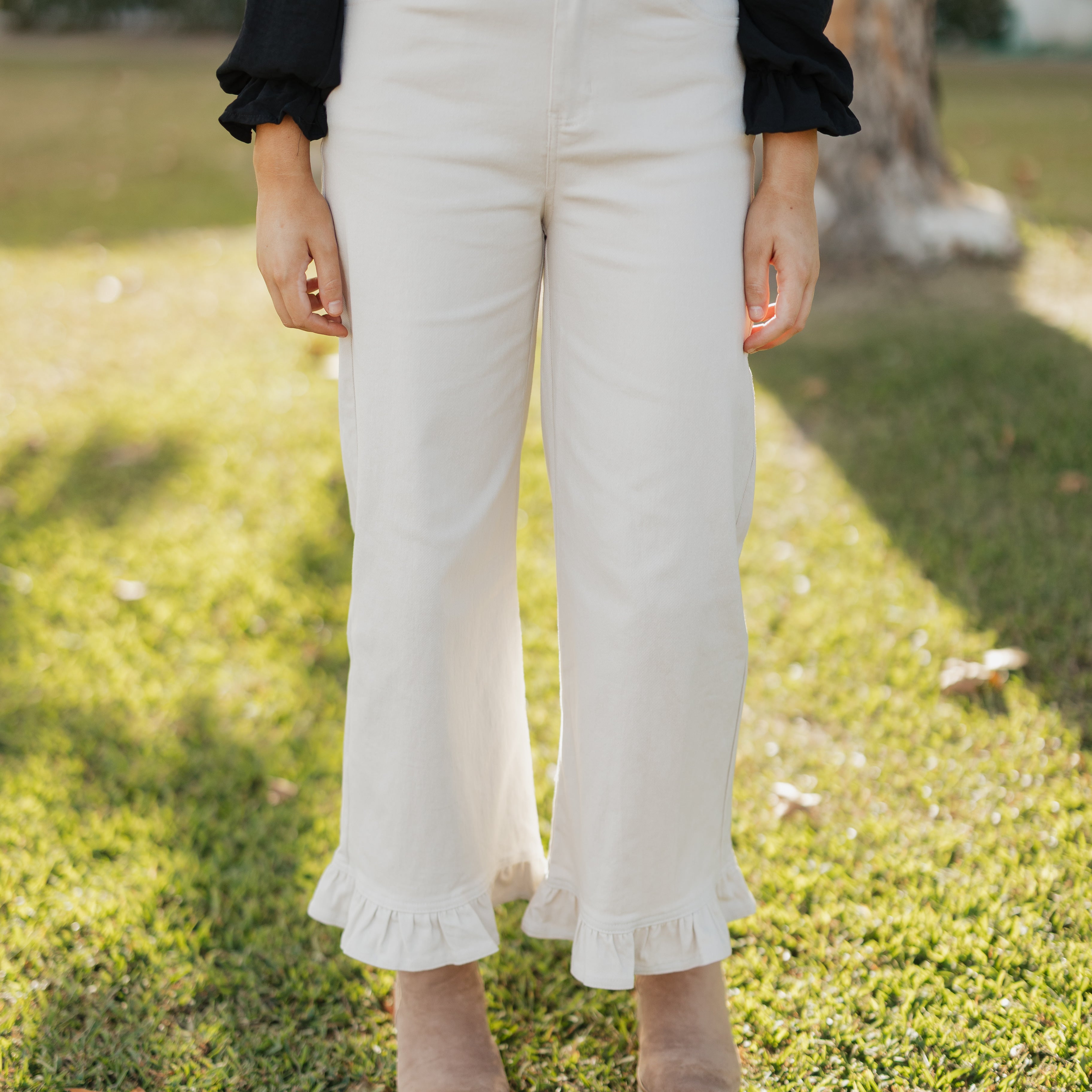 Person wearing sand colored pants with ruffled hem on a grassy background
