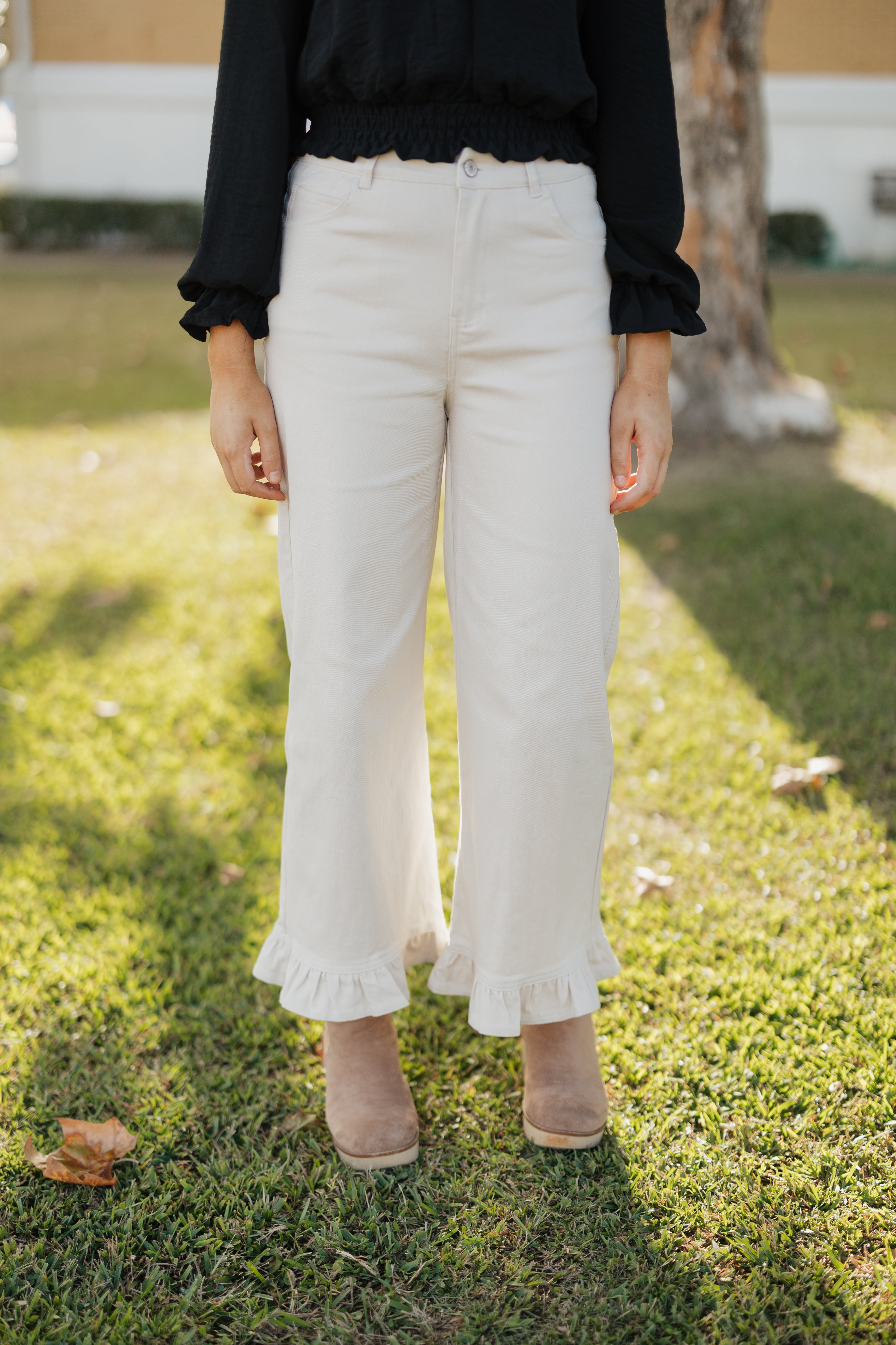 Person wearing sand colored pants with ruffled hem on a grassy background