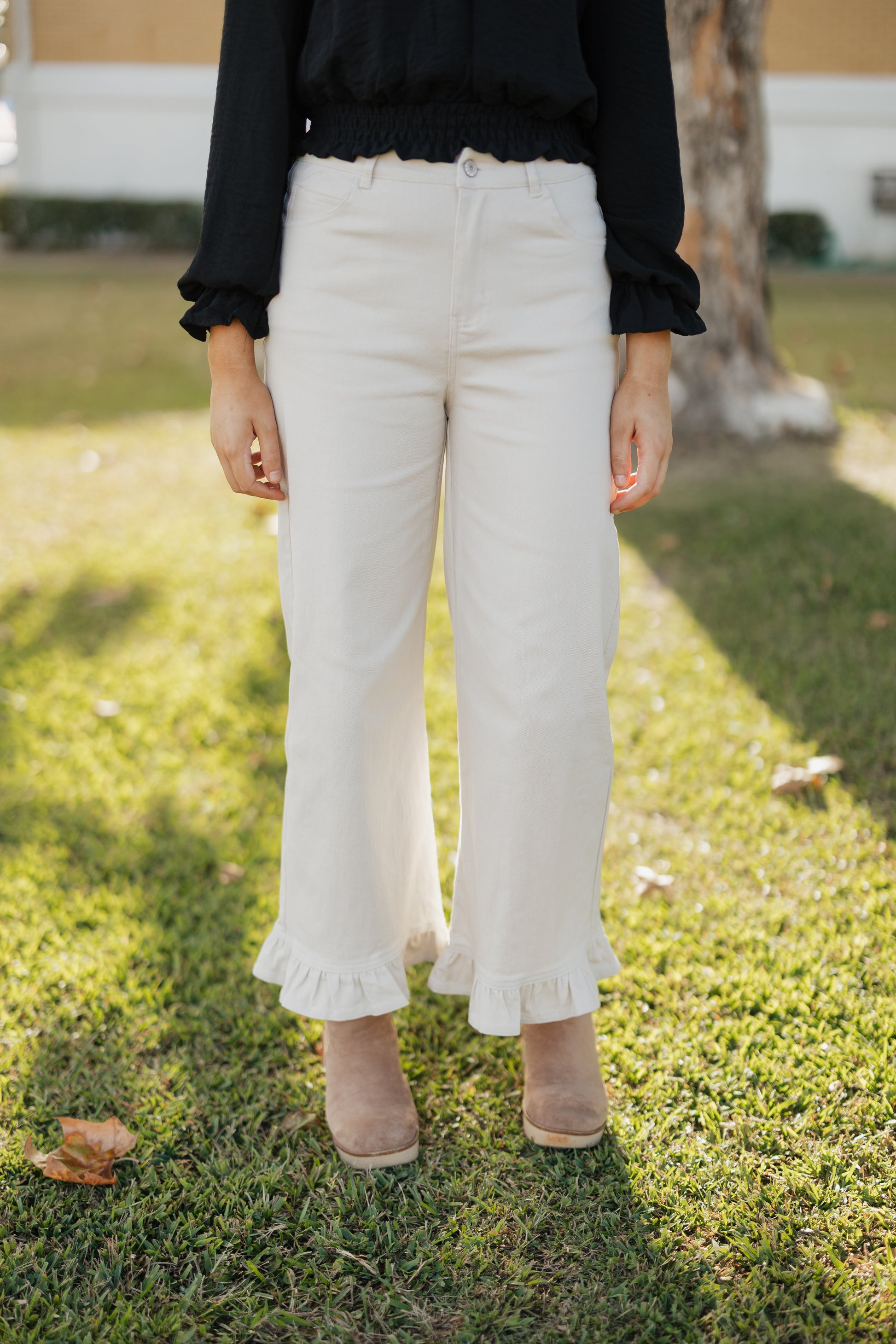 Person wearing sand colored pants with ruffled hem on a grassy background