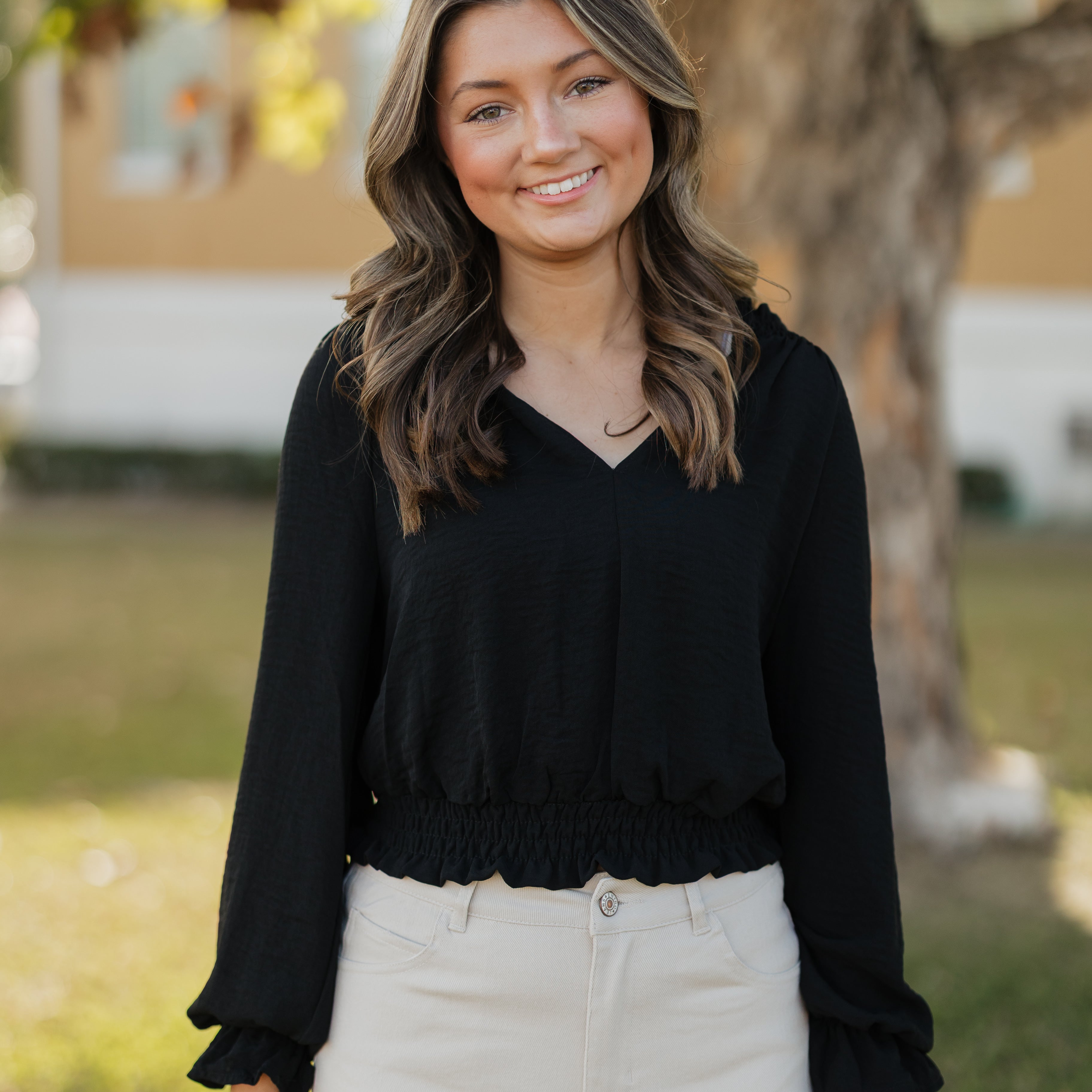 Woman wearing a black top and white pants standing outdoors with a blurred background
