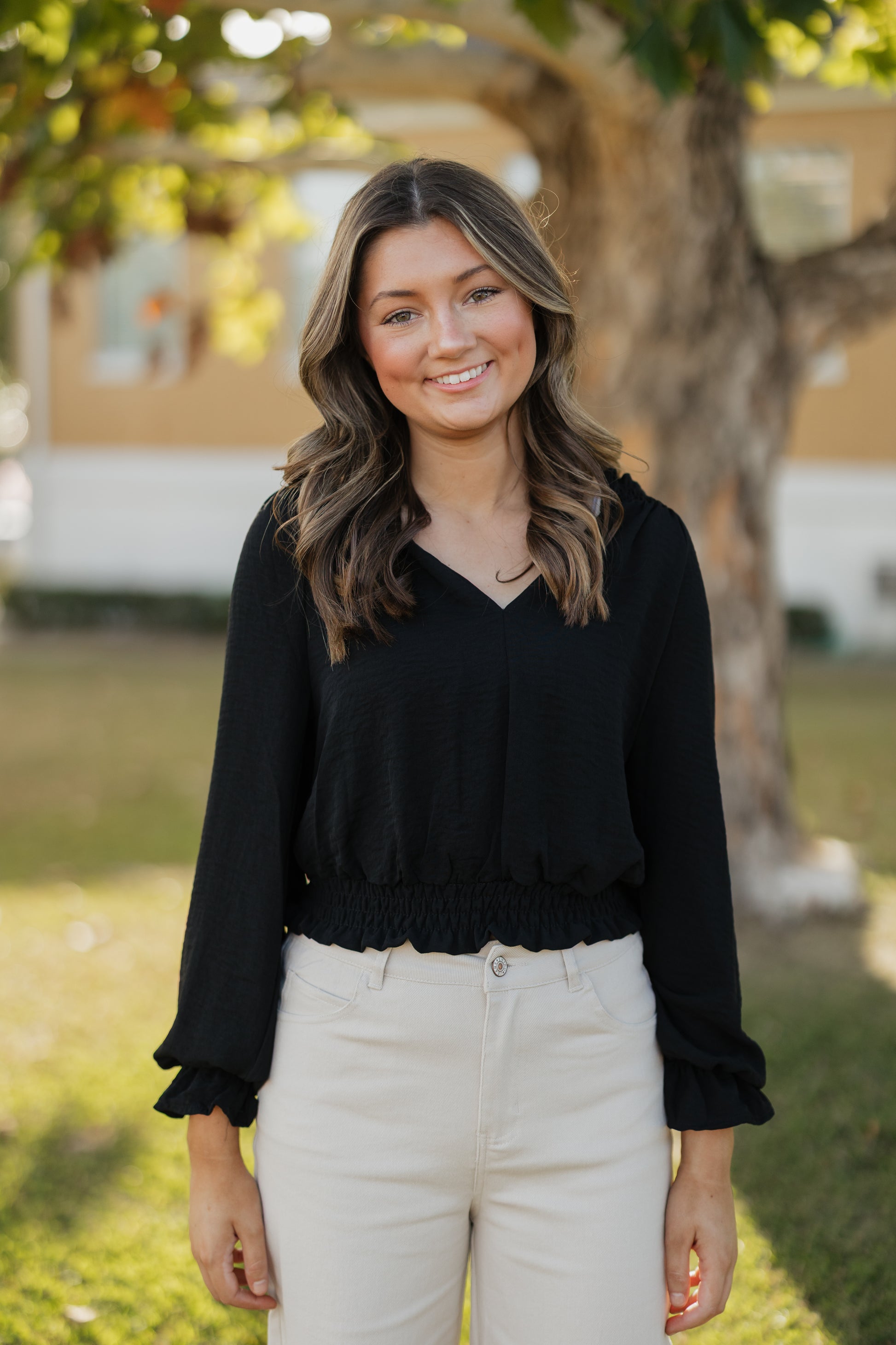 Woman wearing a black top and white pants standing outdoors with a blurred background