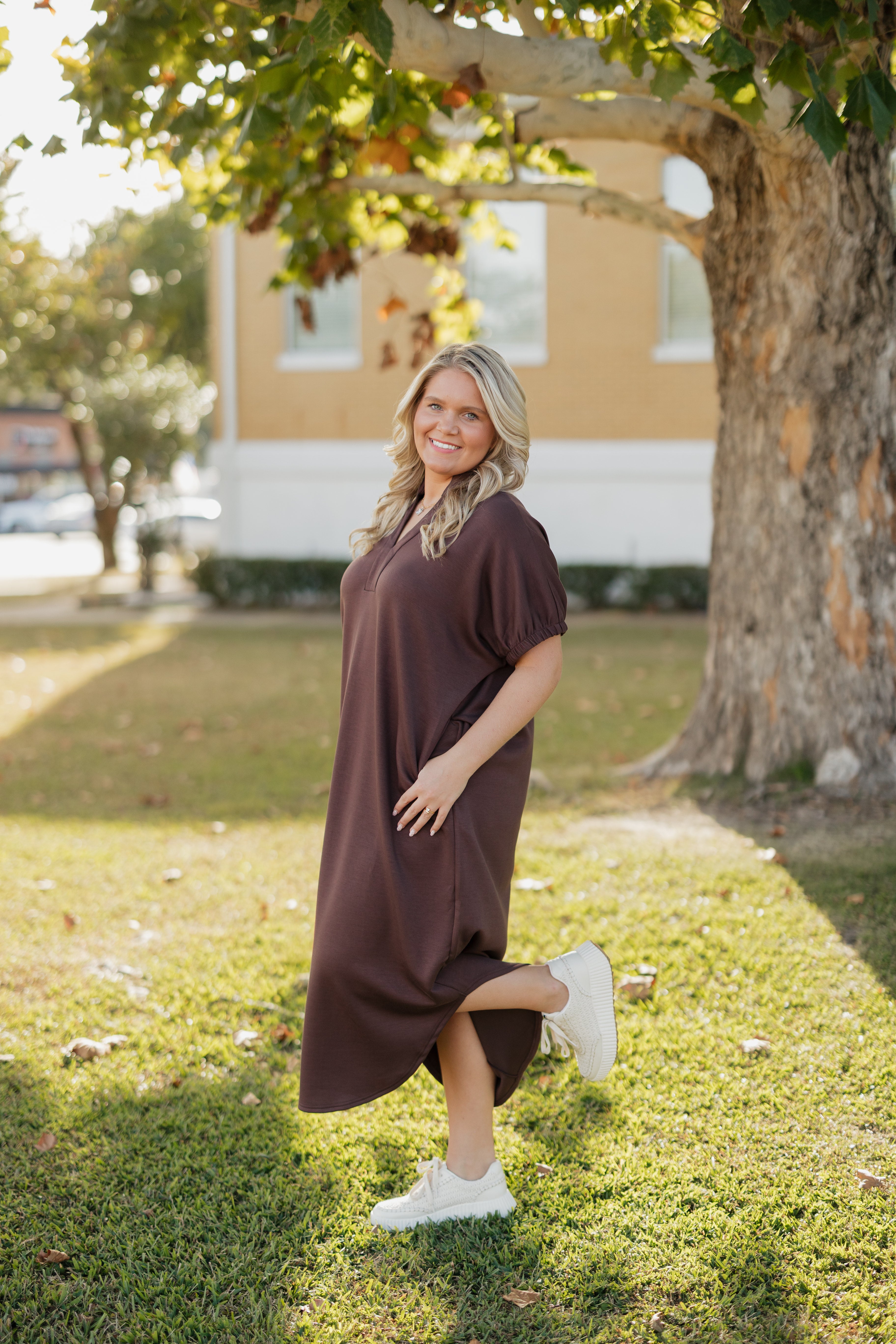Woman in a brown dress standing outdoors near a tree