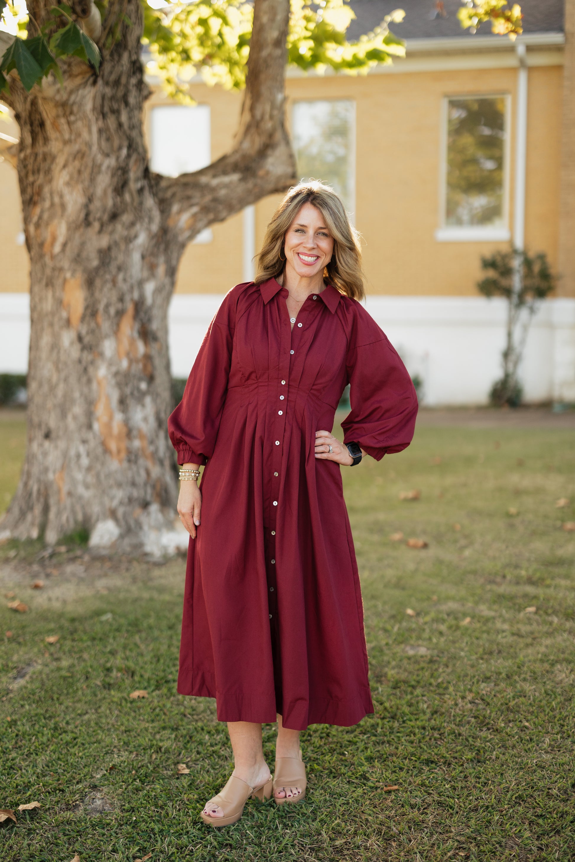 Woman in a garnet dress standing outdoors with a house and tree in the background