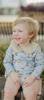 Child wearing a light blue onesie with animal patterns, sitting on a wooden bench outdoors.