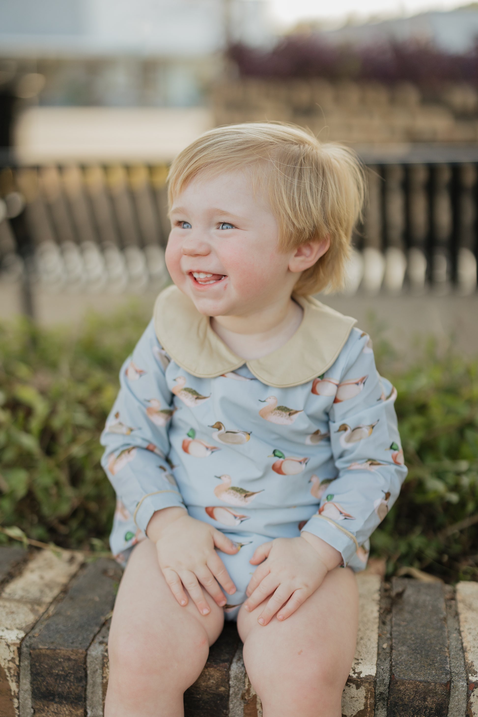 Child wearing a light blue onesie with animal patterns, sitting on a wooden bench outdoors.