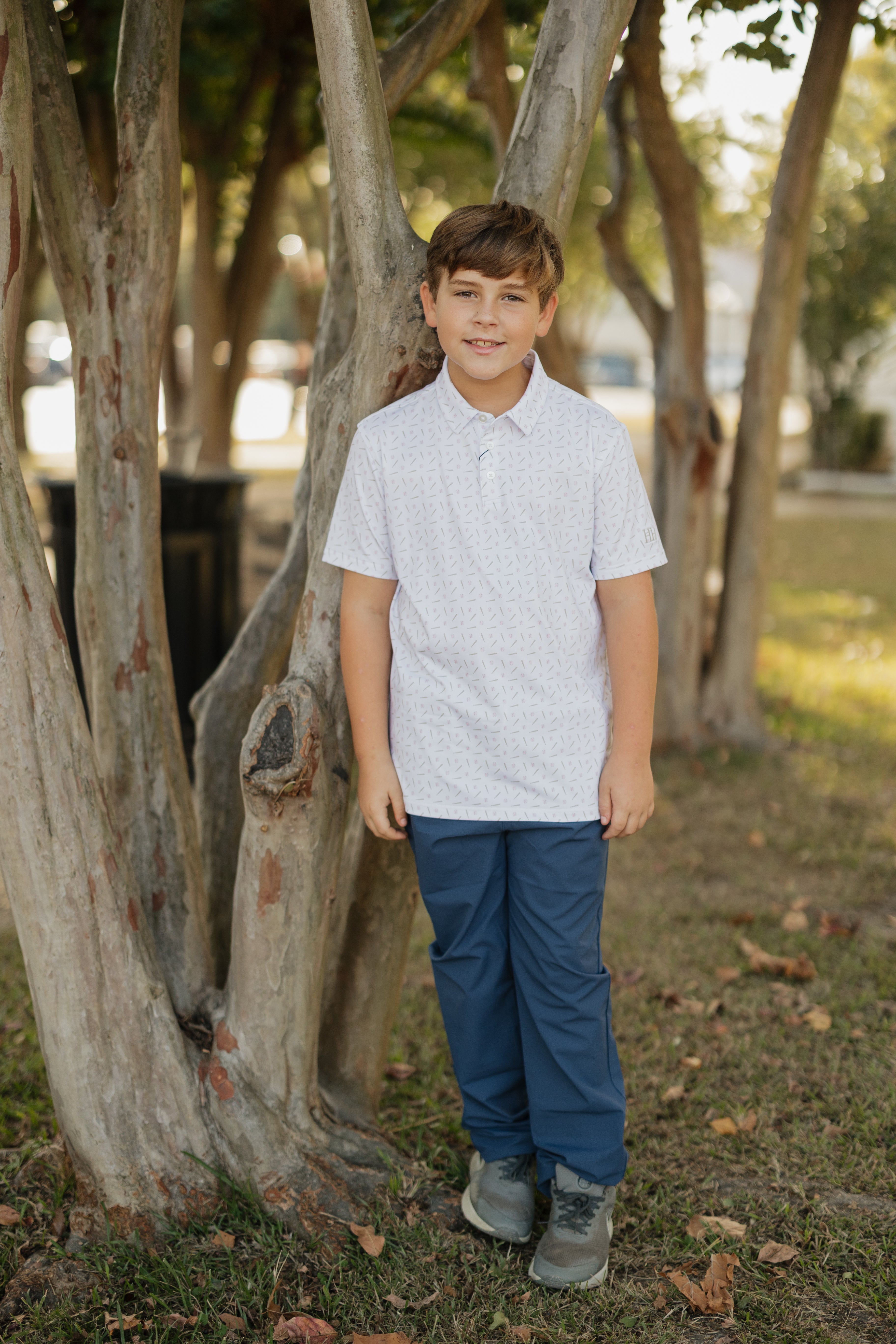 Young boy standing in a park-like setting with trees and grass.