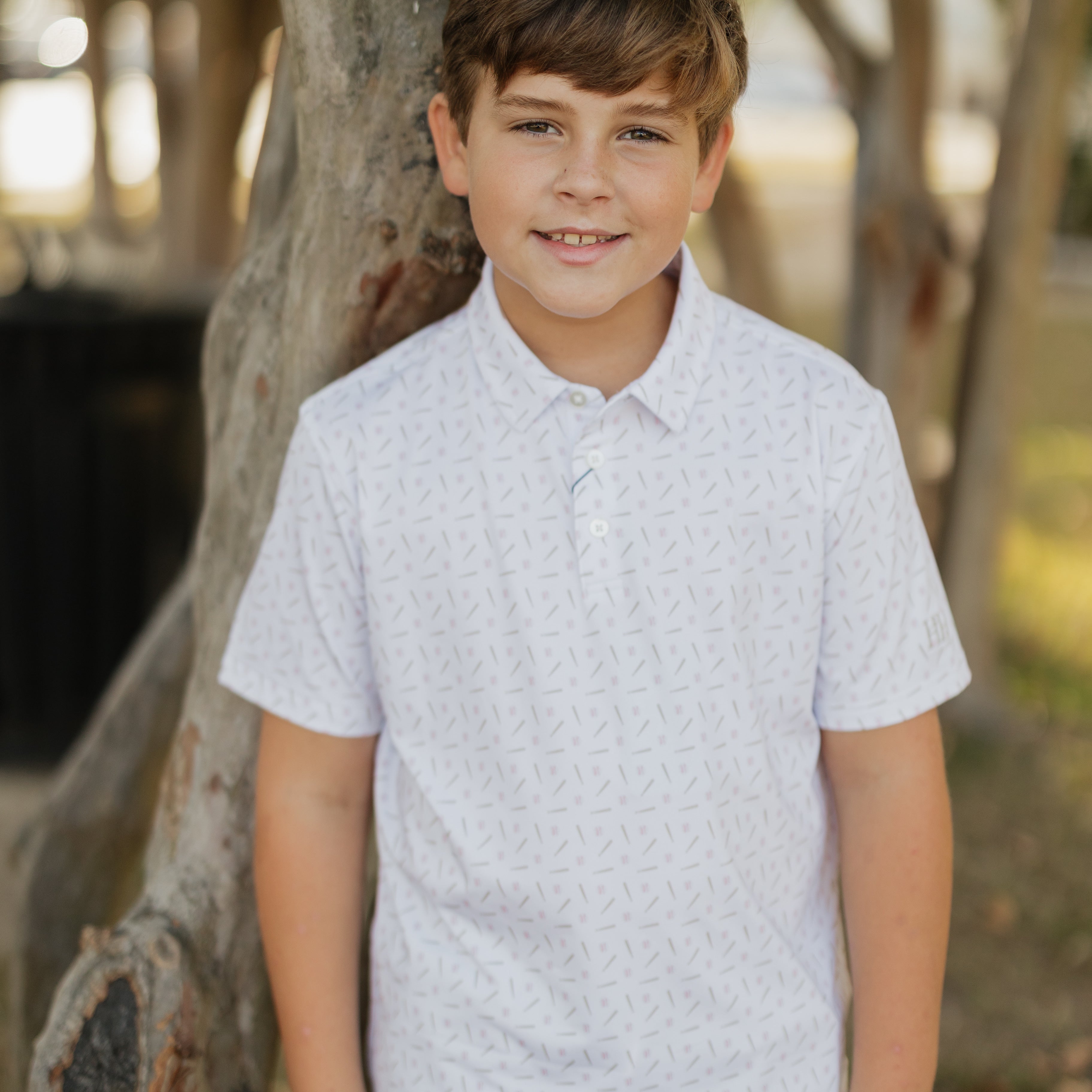 Young boy standing outdoors near a tree with a blurred background