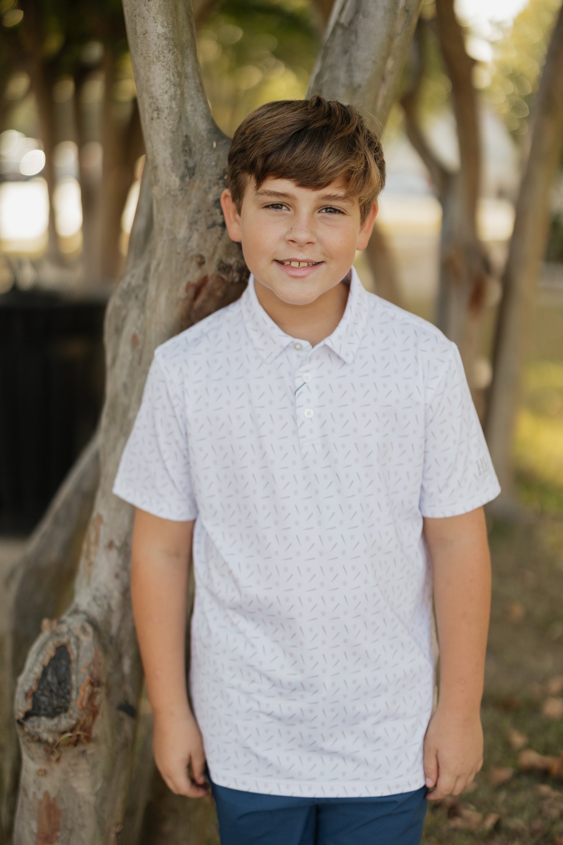 Young boy standing outdoors near a tree with a blurred background
