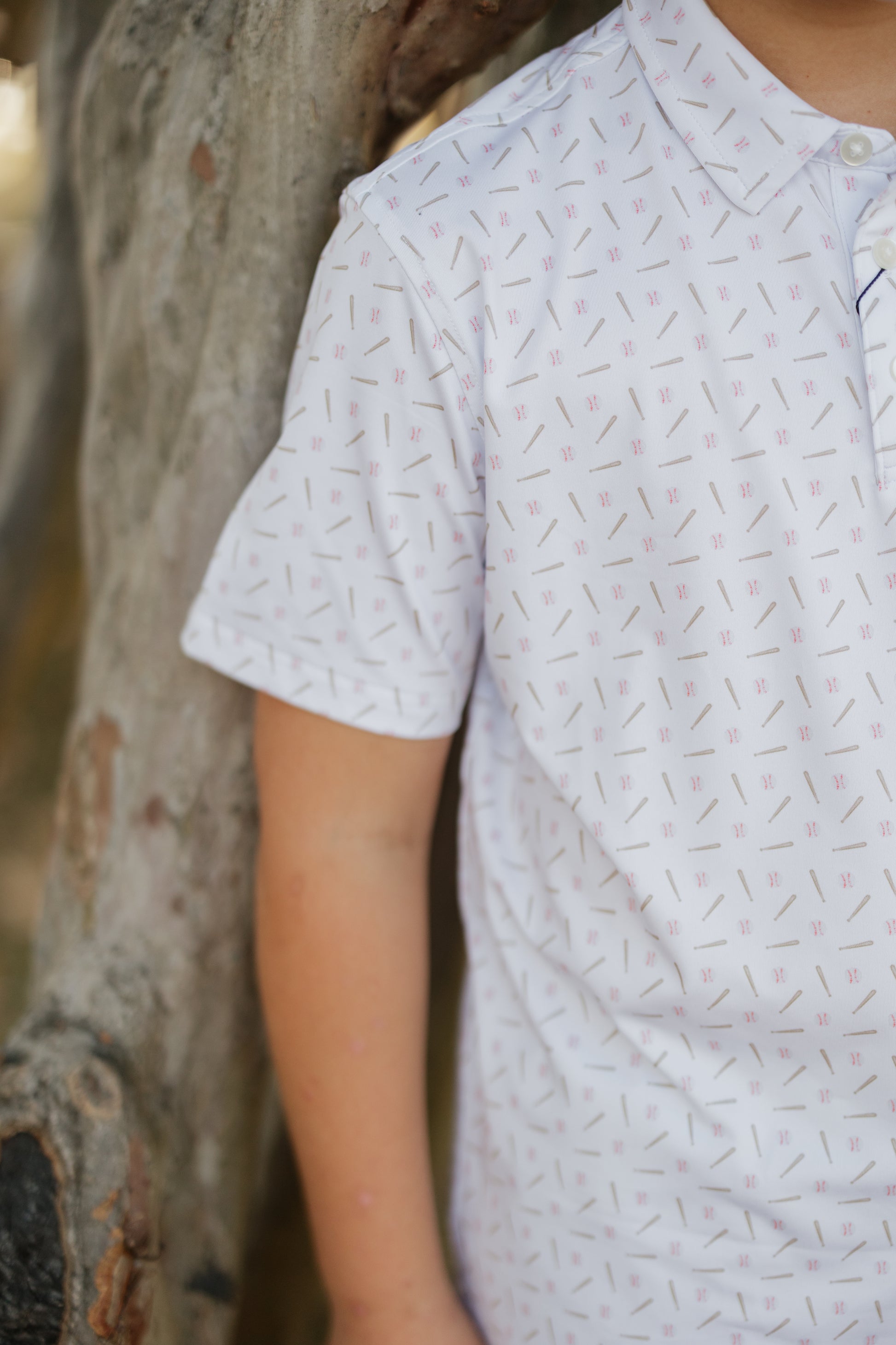 Person wearing a light gray patterned shirt standing next to a tree.